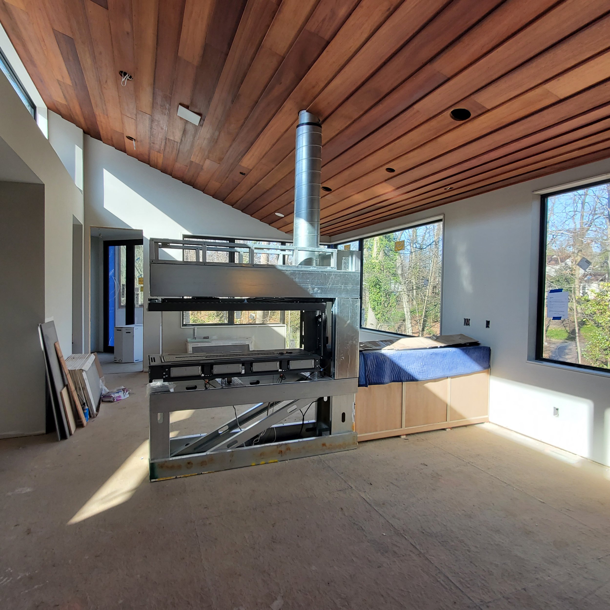 Three-sided gas fireplace unit in steel framing beneath the finished salvaged mahogany ceiling at Hadro House Haddonfield NJ, March 2021 — two signature elements meeting mid-construction