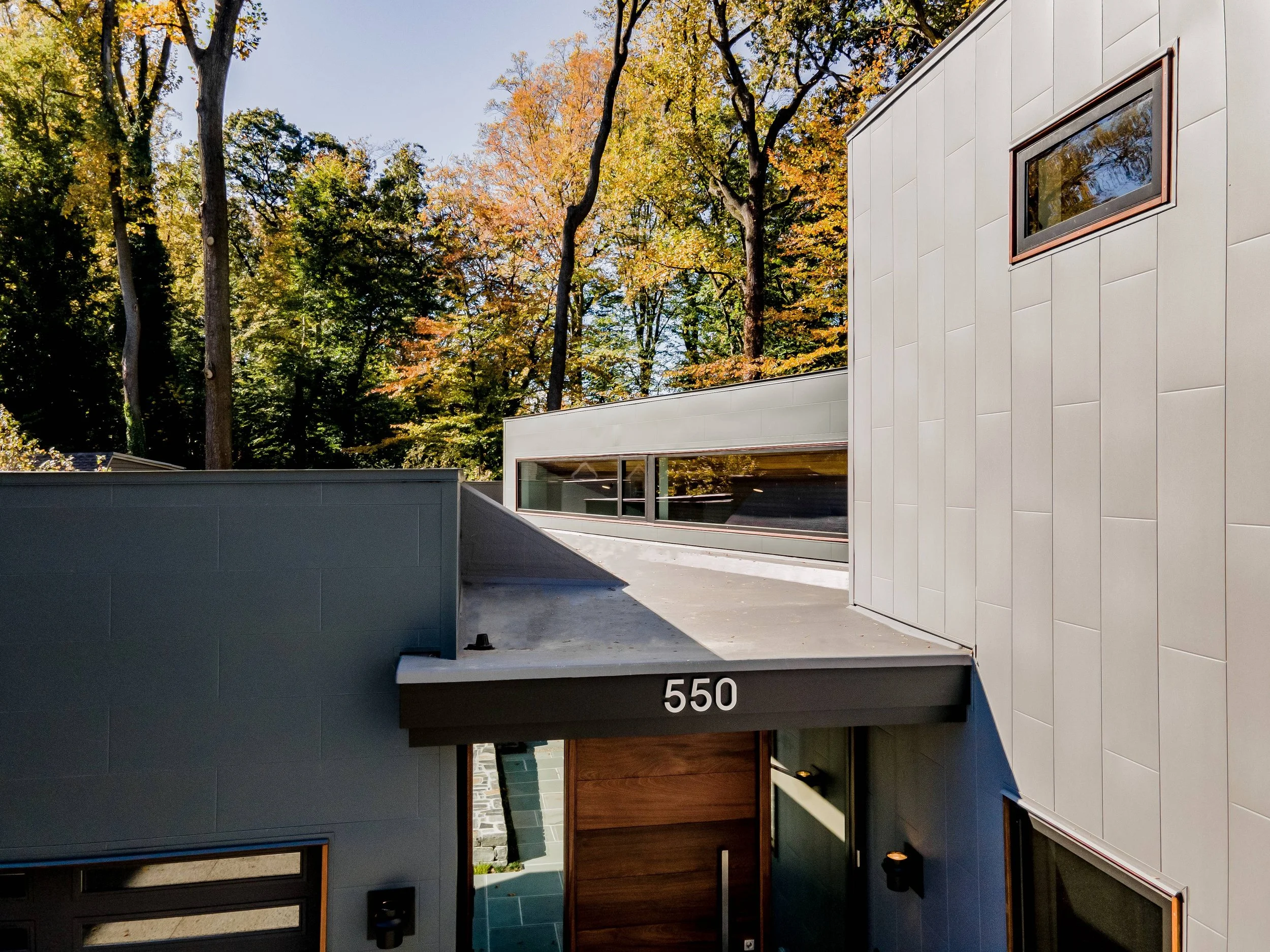 Wood pivot entry door of Hadro House Haddonfield NJ set between textured steel panels installed in alternating orientations, referencing the running-bond brick of the neighborhood