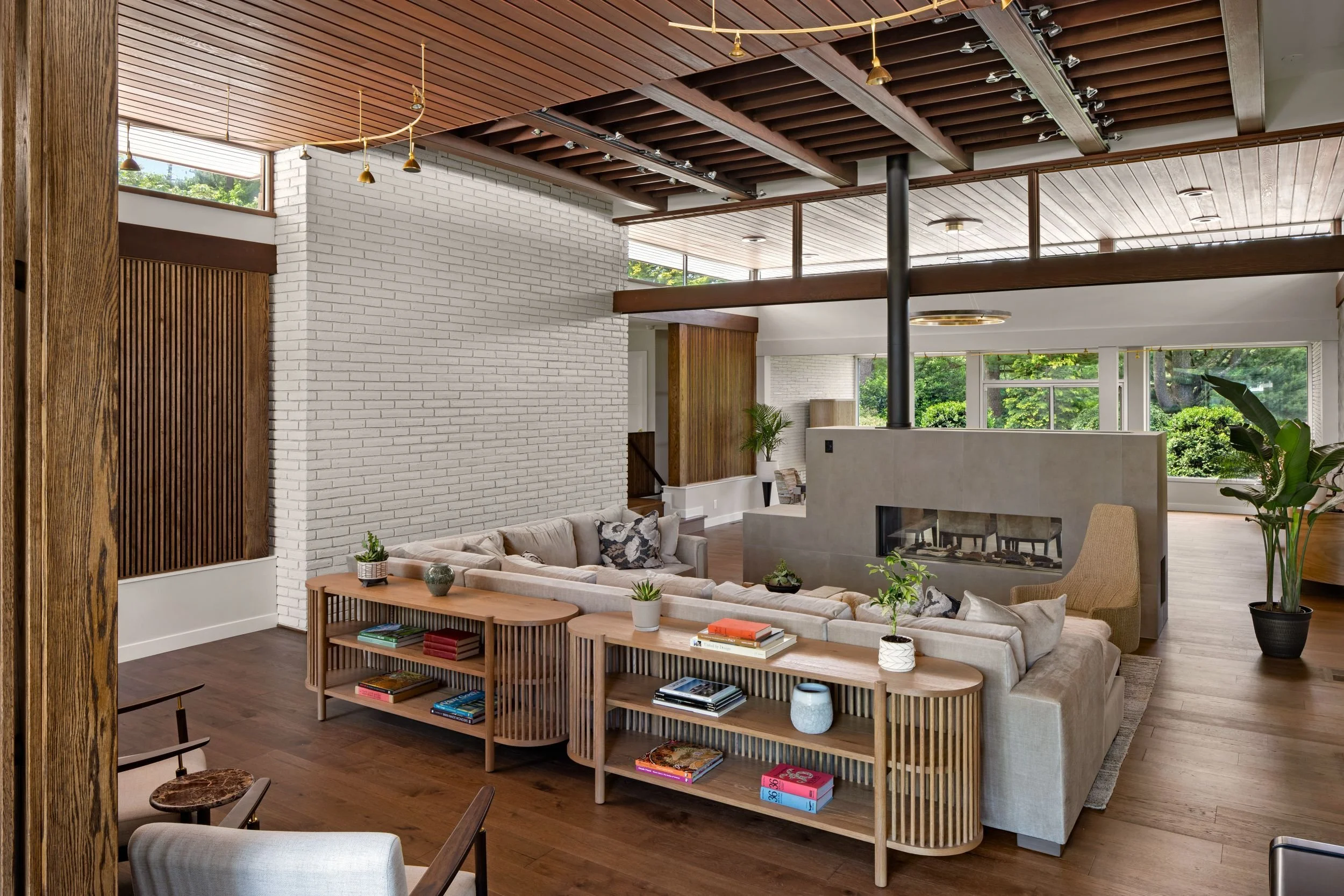 Renovated mid-century modern living room in Cherry Hill, NJ with floating two-sided fireplace, white brick walls, clerestory windows, wood ceiling, exposed beams, and oak slat details.