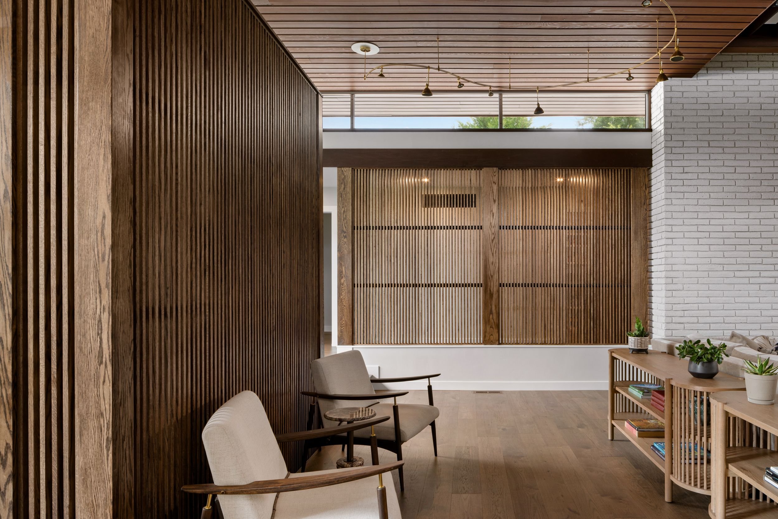 Renovated mid-century modern entry corridor Cherry Hill NJ — oak slat screen detail close up clerestory windows wood ceiling mid-century chairs brass pendants layered arrival sequence J Reinert Architecture