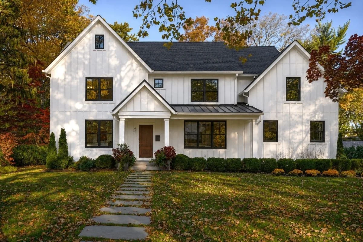 White House Black Windows Shadow custom new home Haddonfield NJ — white board and batten siding black fiberglass windows standing seam metal entry porch roof warm wood front door autumn landscaping J Reinert Architecture