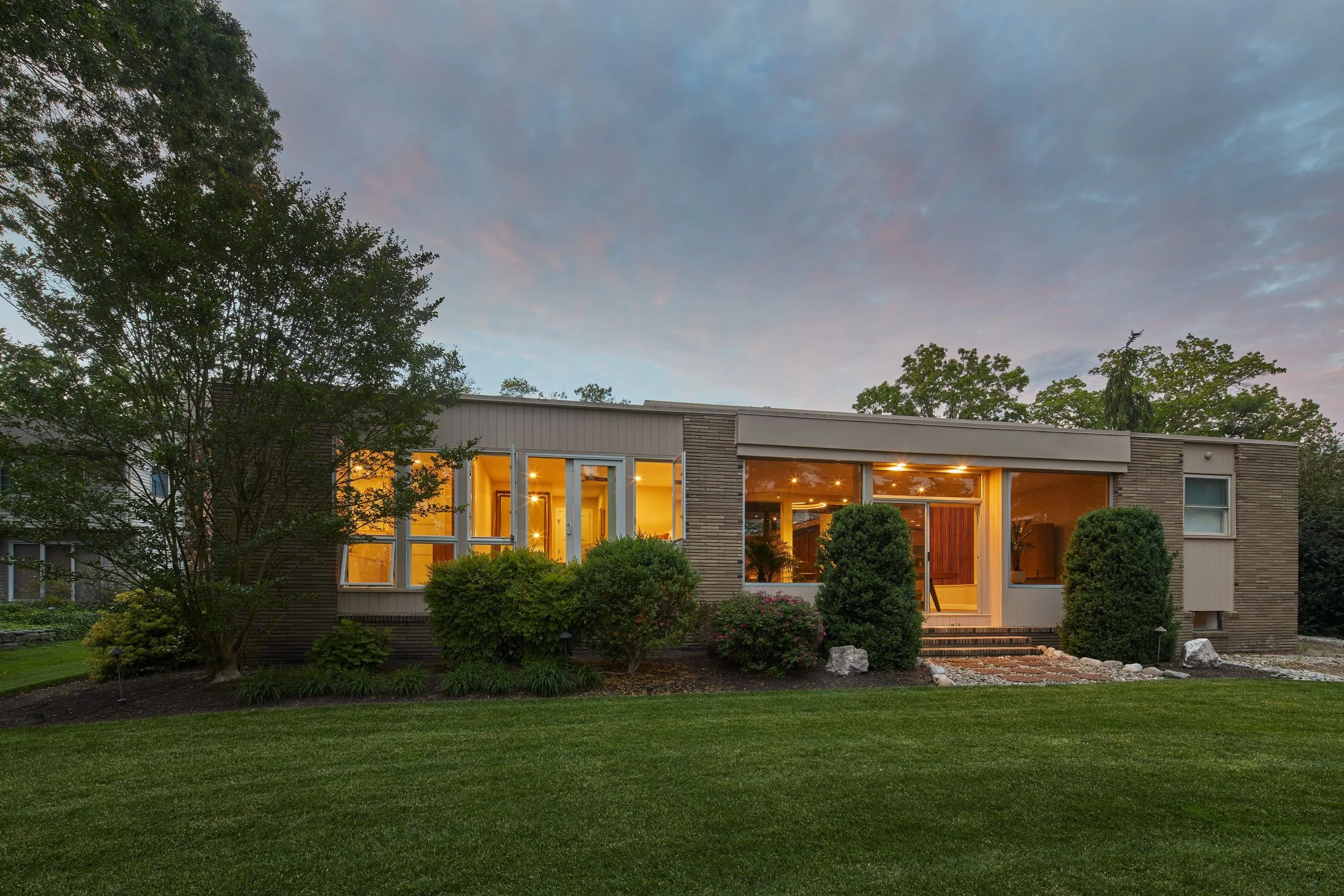 Renovated 1964 mid-century modern home Cherry Hill NJ rear elevation dusk — enclosed porch reopened integrated into living volume original masonry restored full rear glazing golf course views J Reinert Architecture
