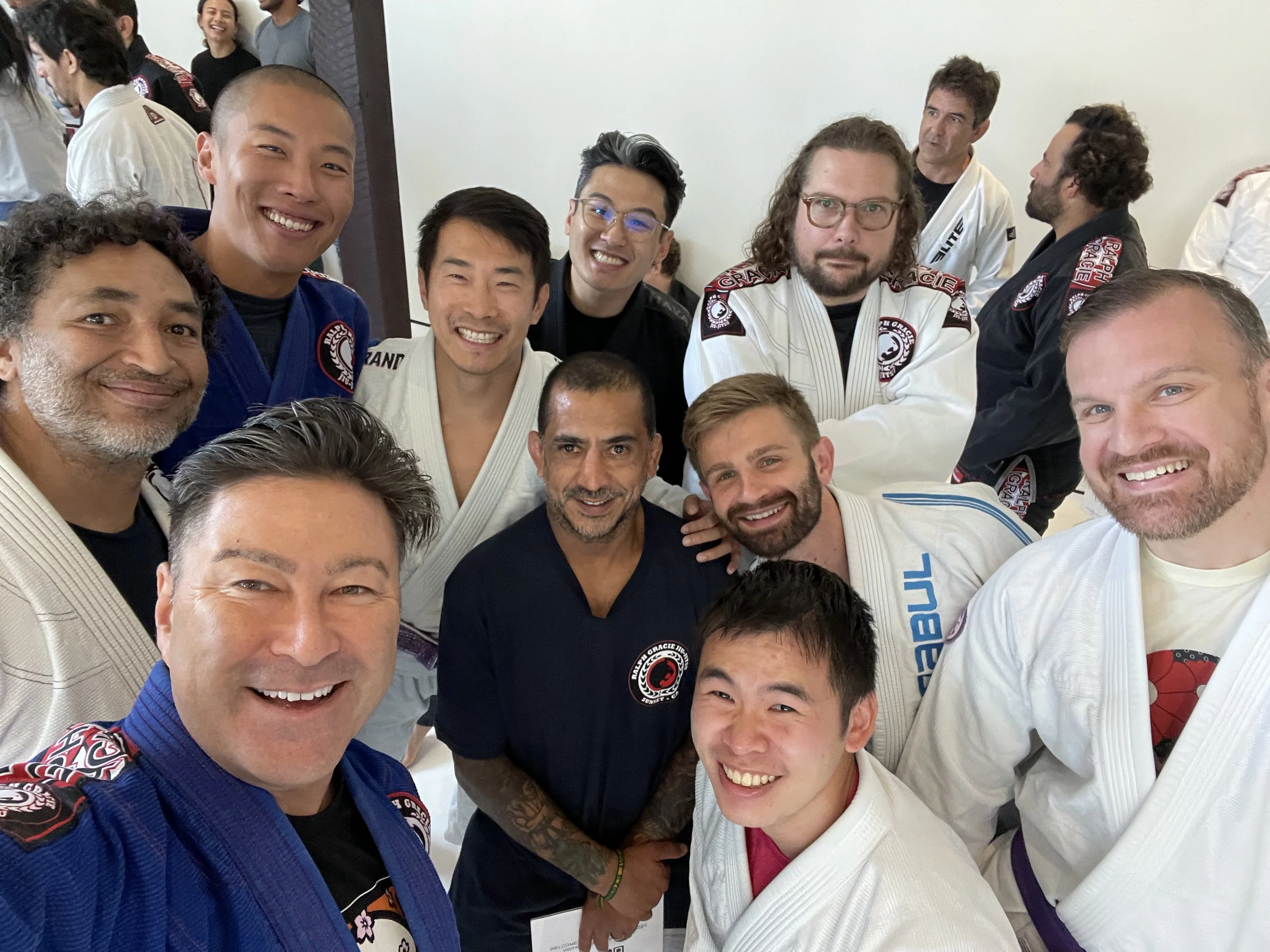 Group of martial artists in gis, smiling and taking a selfie in a training room.