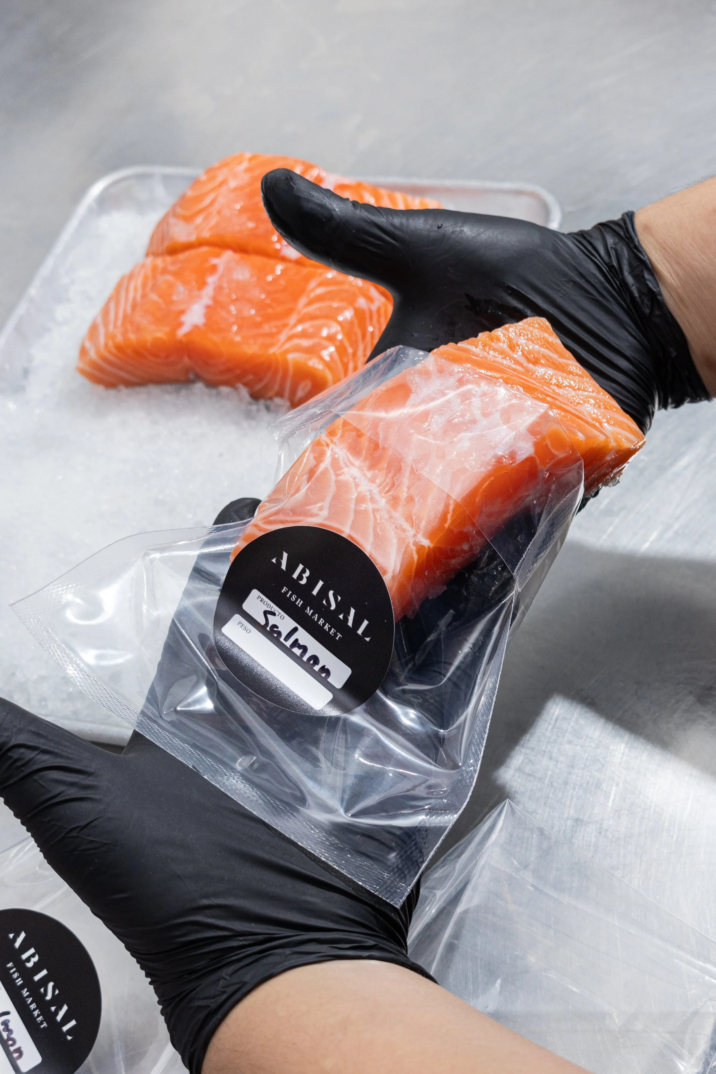 Fresh raw salmon fish fillets on a bed of ice with a person's hand in black gloves holding one of the fillets in clear packaging from a fish market.