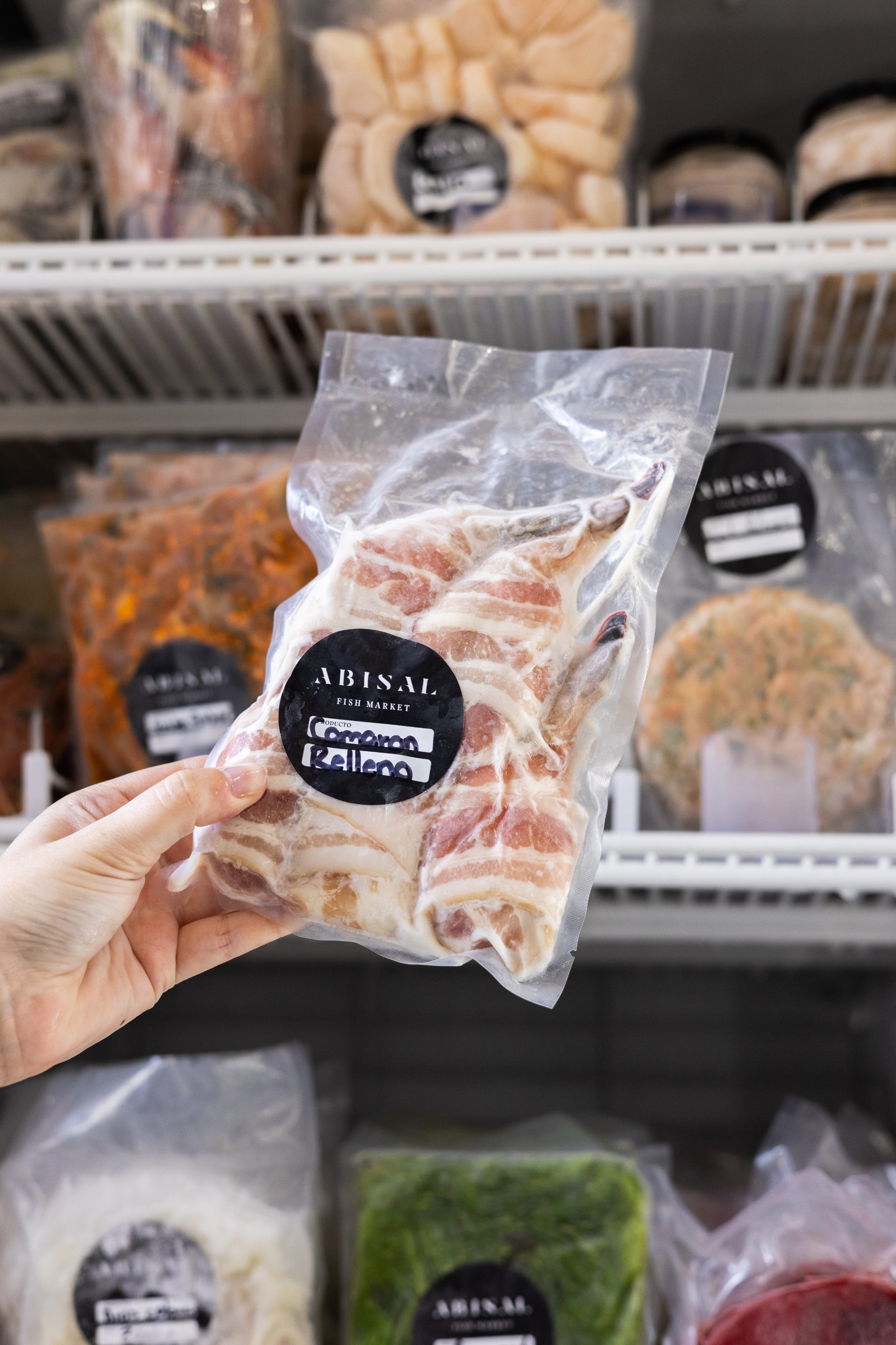 A person holding a vacuum-sealed package of pork belly in front of a refrigerated shelf at a grocery store.