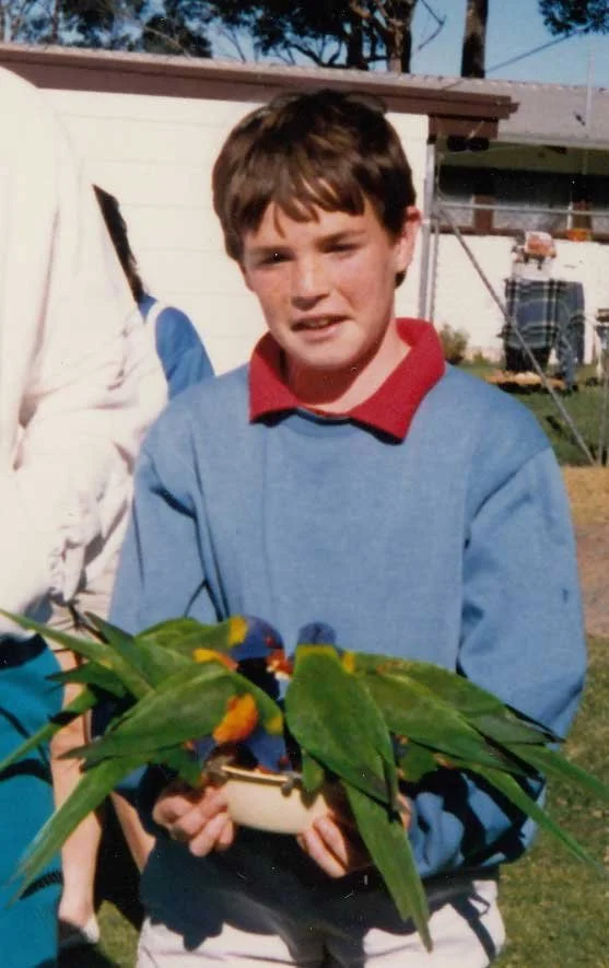 Young David making a face as rainbow lorikeets eat from a bowl in his hands