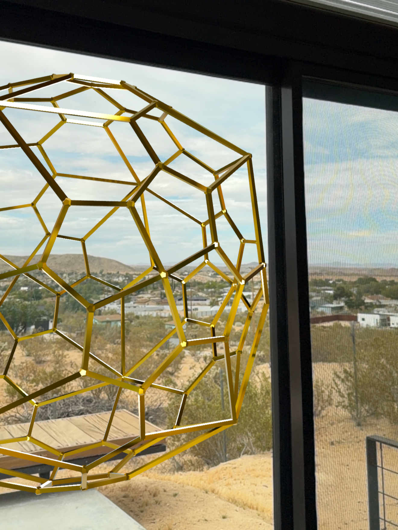 A golden geometric floating Geb Astra shape, placed outside of a large window with a view of a desert landscape with hills and sparse vegetation.