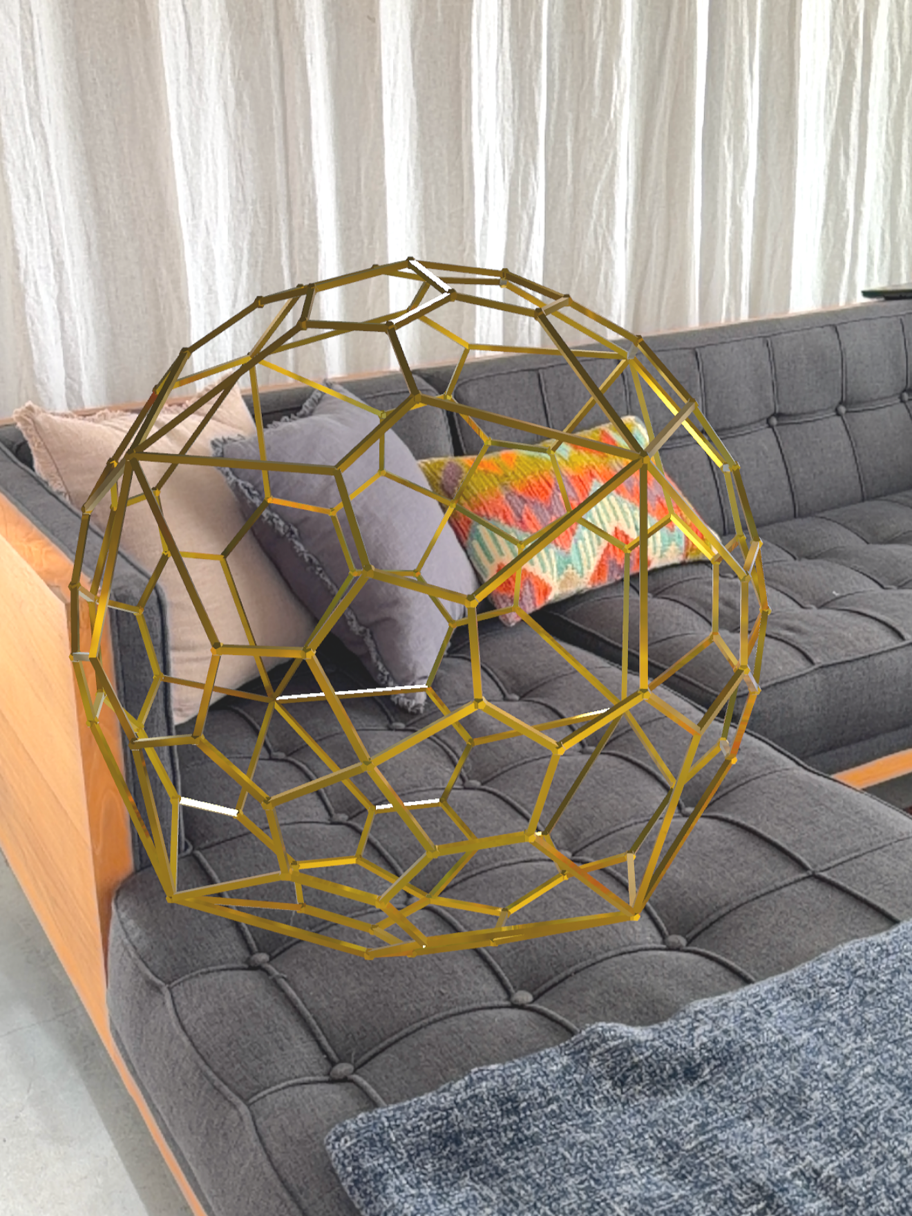 Living room with a gray tufted sofa, colorful throw pillows, a patterned blanket, and a gold geometric Geb Astra shape in the foreground.