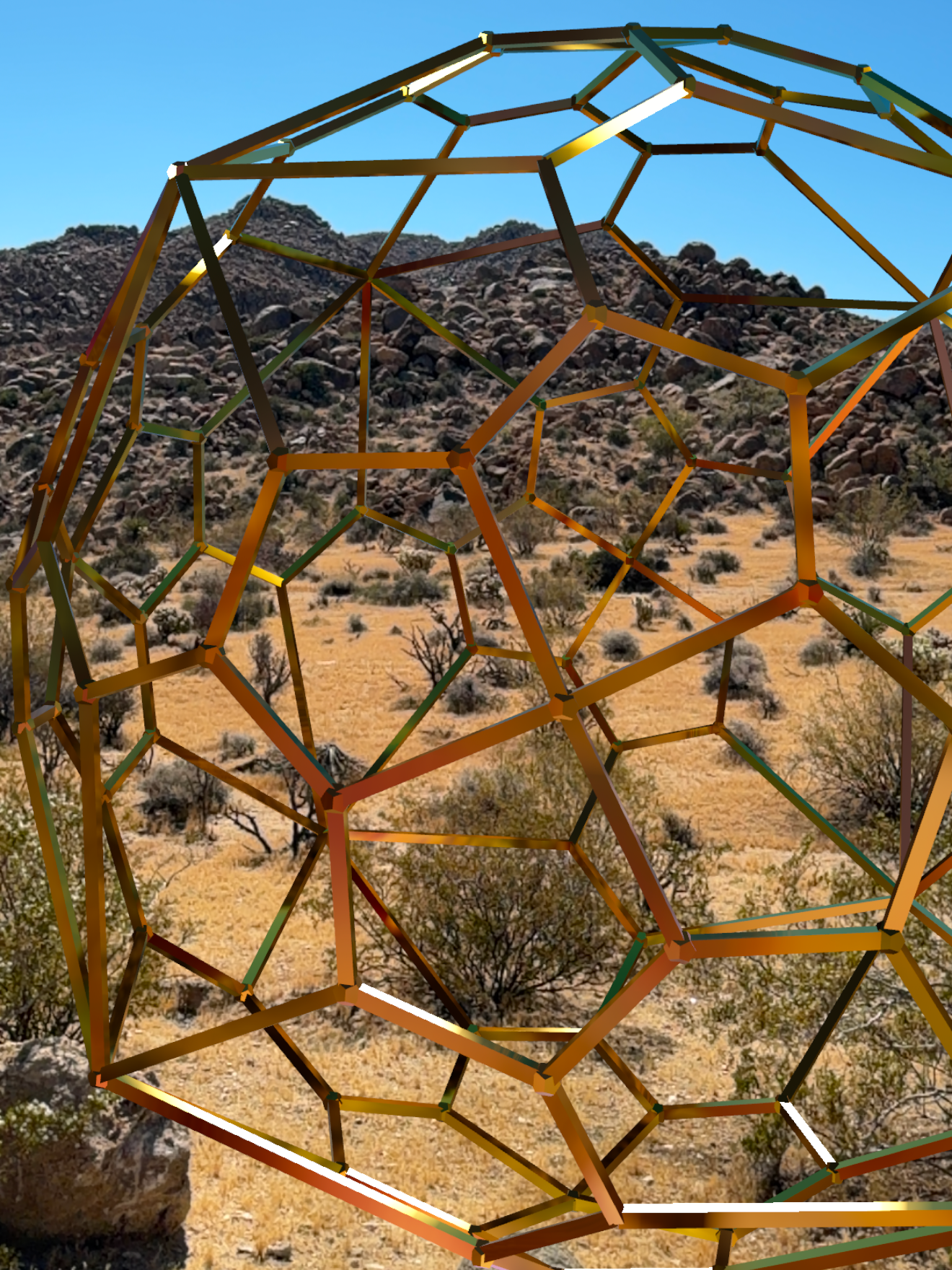 A geodesic dome structure made of metal rods set against a desert landscape with mountains and sparse vegetation under a clear blue sky.