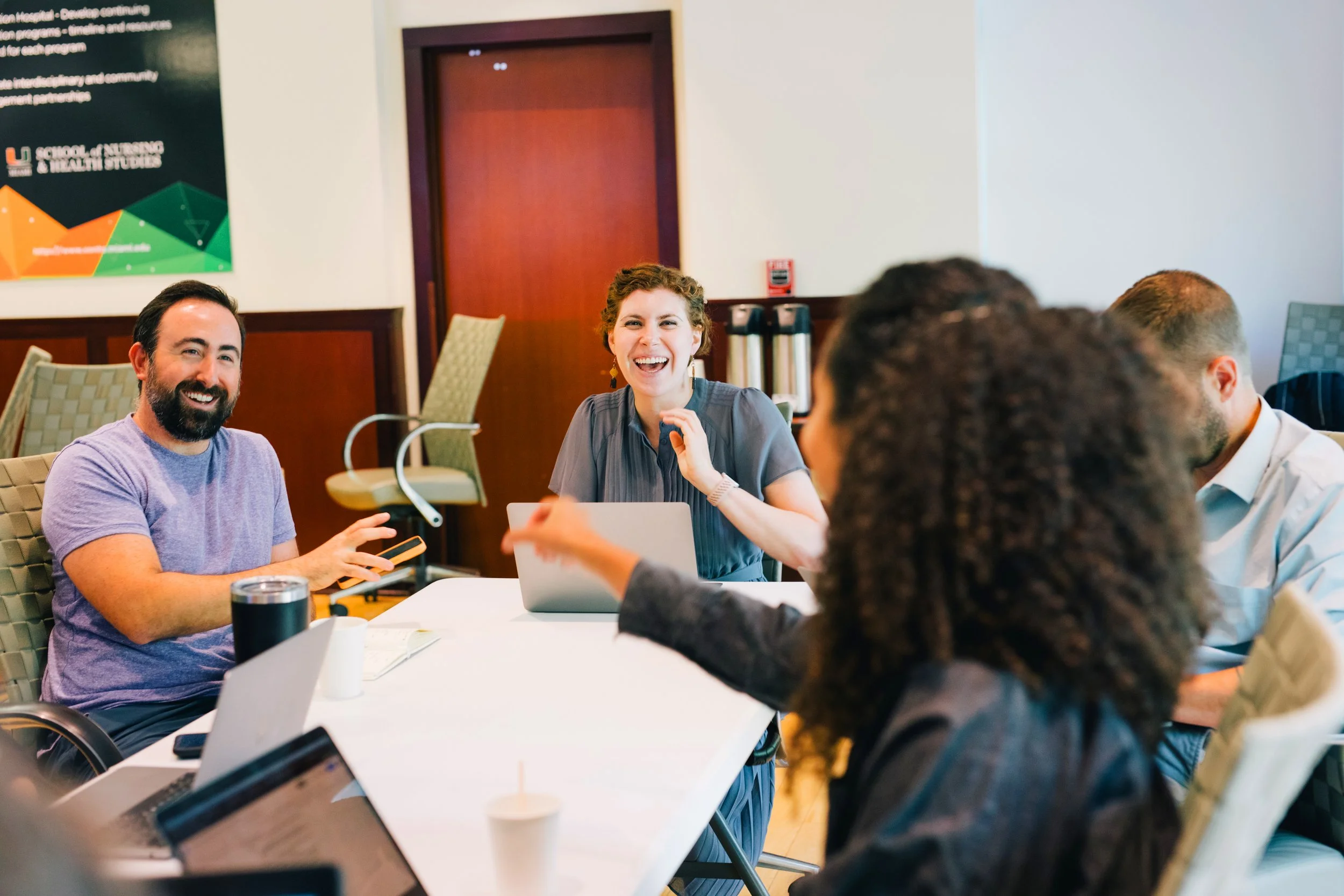 Diverse group of coworkers smiling and collaborating around a conference table with laptops in an office