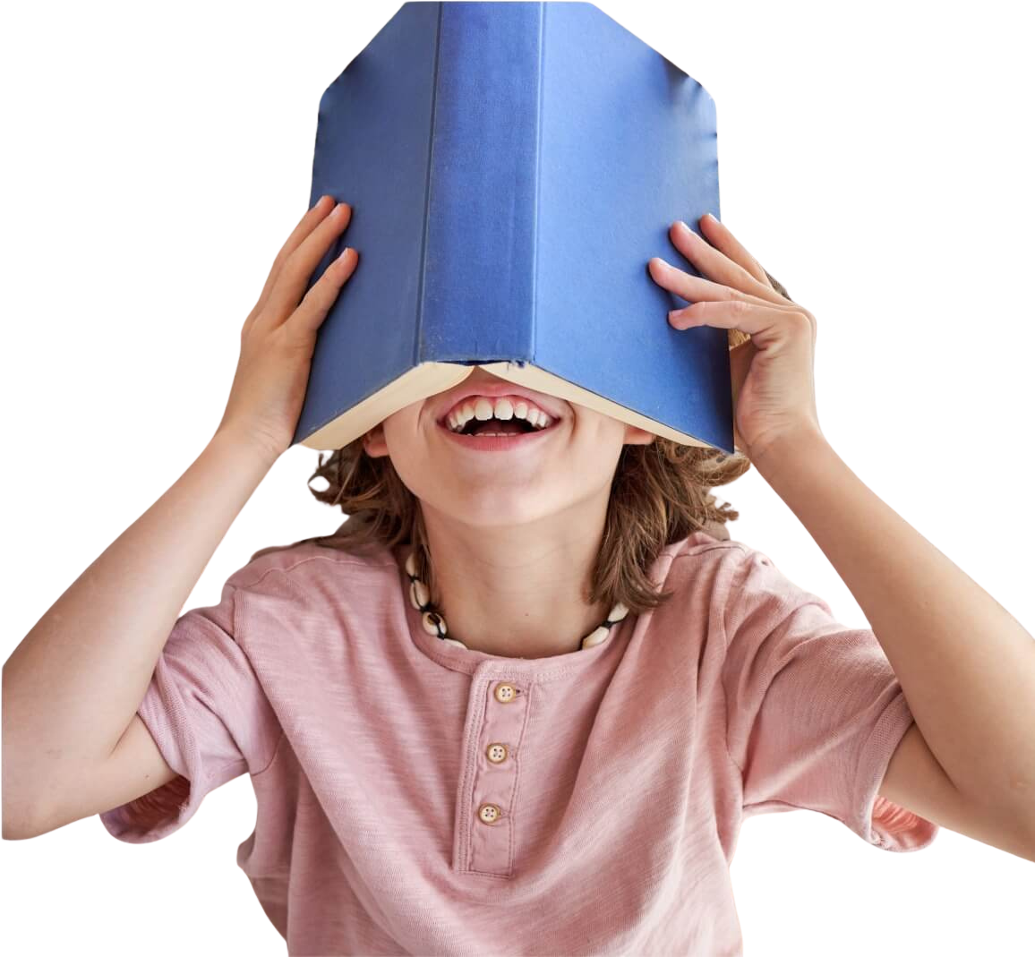 Child with shoulder-length hair and a pink shirt smiling, holding a blue book over their face like a mask.