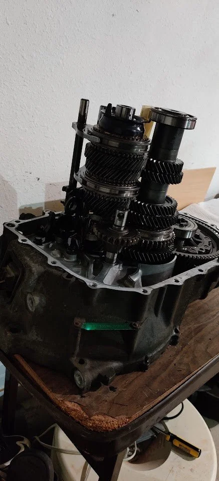 Disassembled car transmission with gears inside a metallic casing on a wooden table.