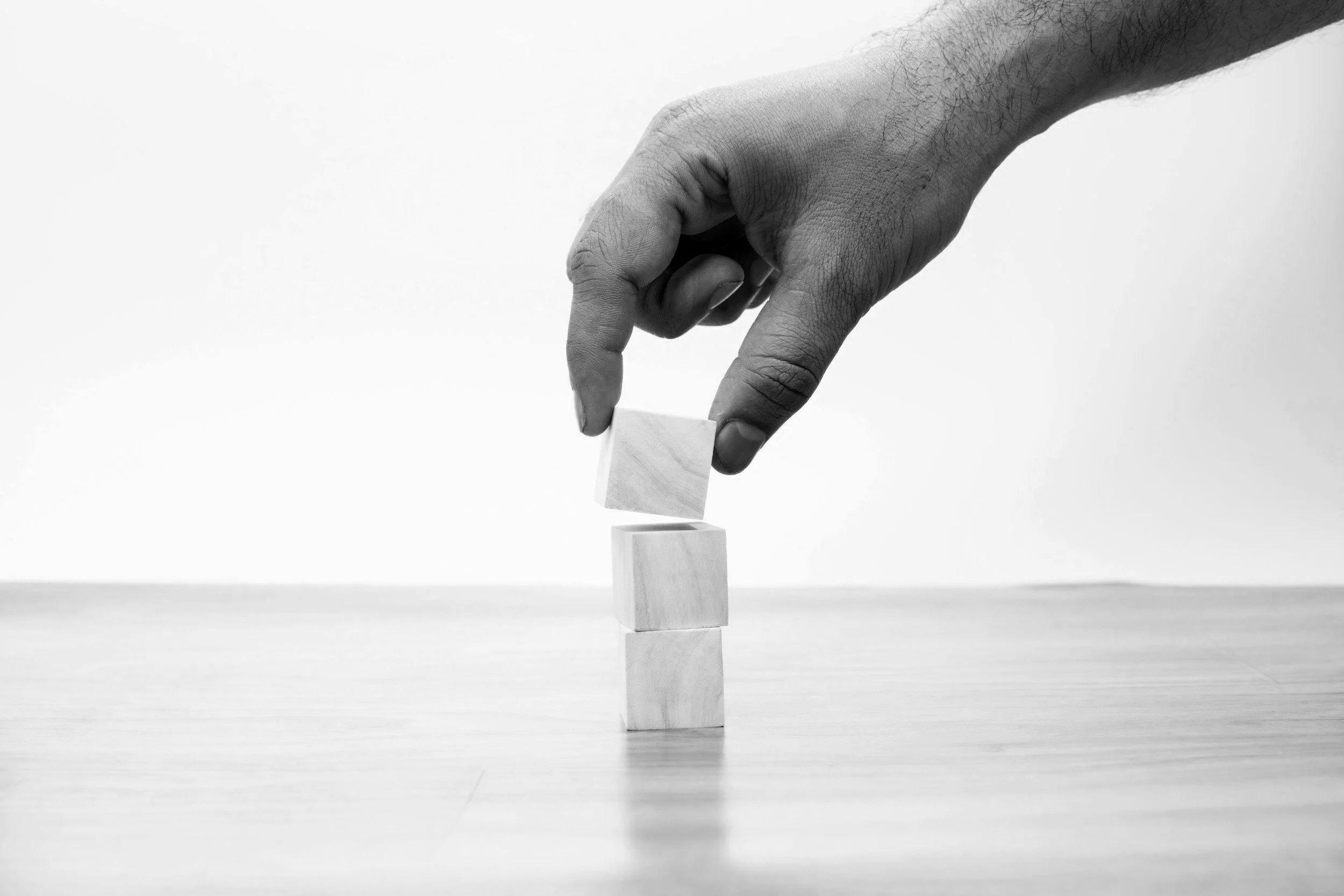 Hand stacking blocks representing practical steps and operational improvement.