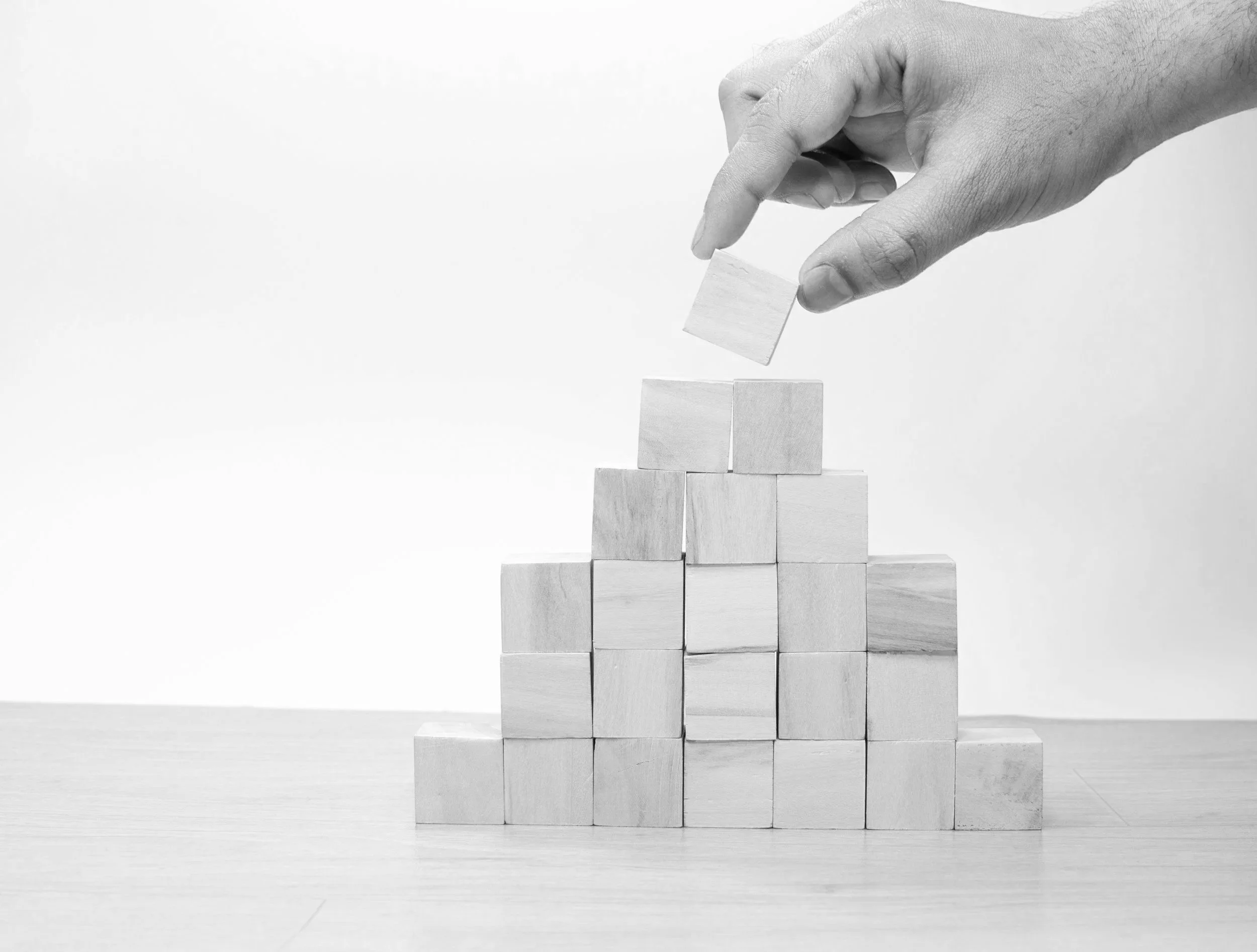 A hand stacking wooden blocks to form a pyramid.