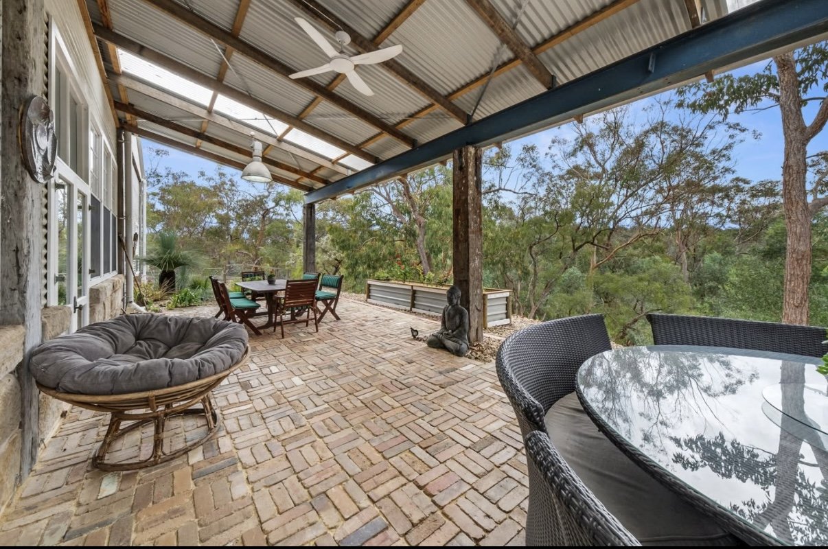 Outdoor patio with wicker furniture, a dining table, and a lounge chair, surrounded by trees.