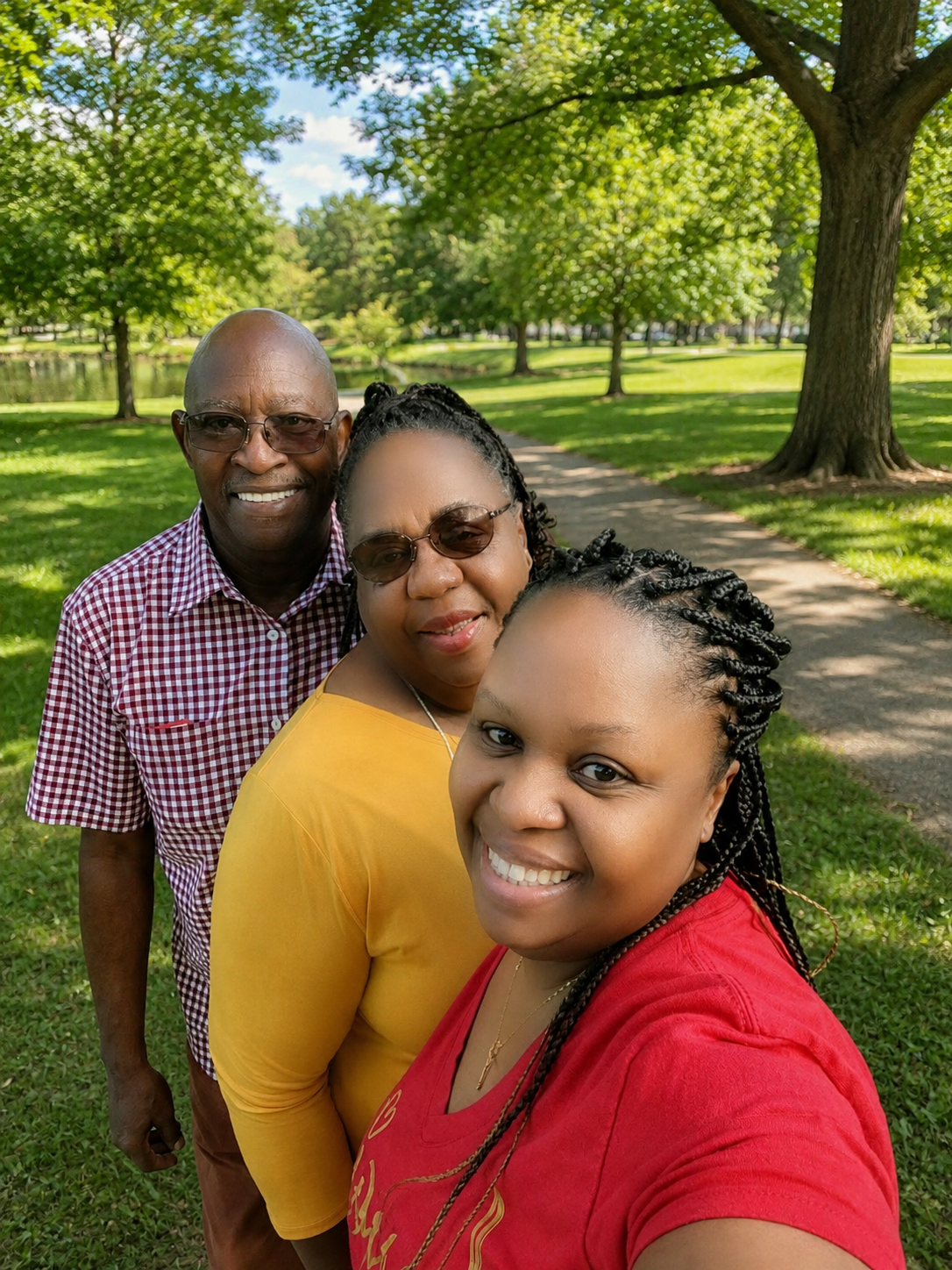 A family of four taking a selfie in a park with green trees, grass, and a pathway.