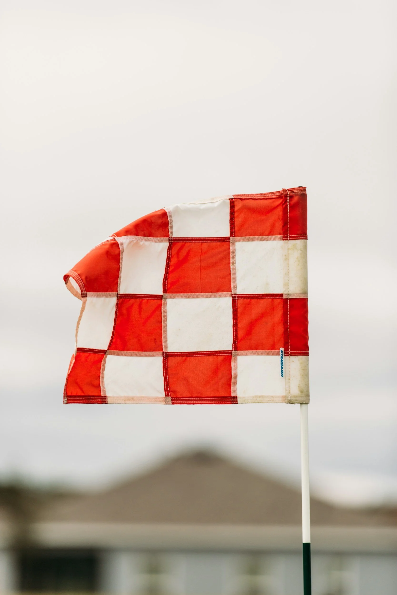 Race flag with red and white checkered pattern on a golf flagstick, set against a white background.