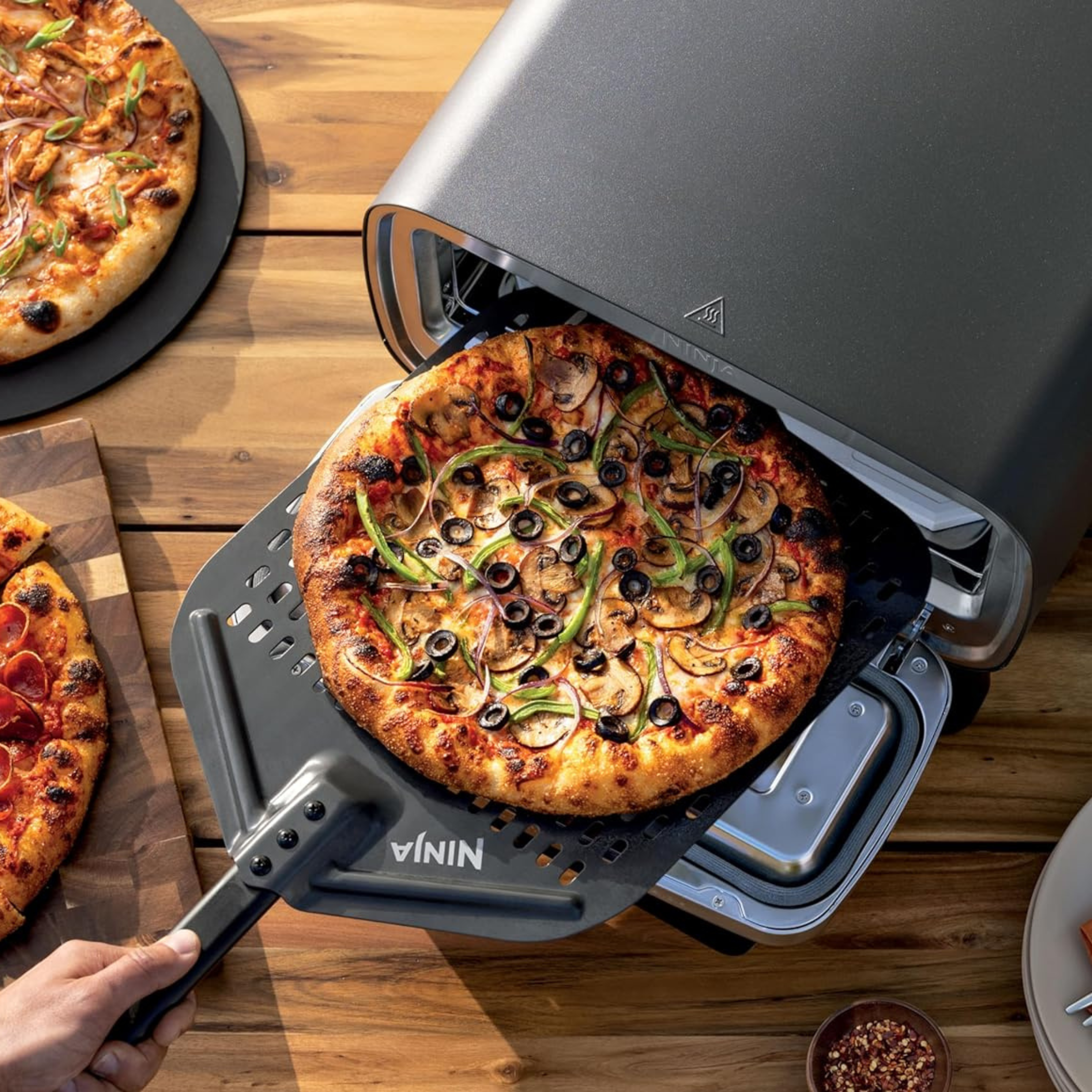 Ninja Artisan outdoor pizza oven with freshly baked pizza on a wooden table — backyard hosting investment pick curated by The Alcove Edit