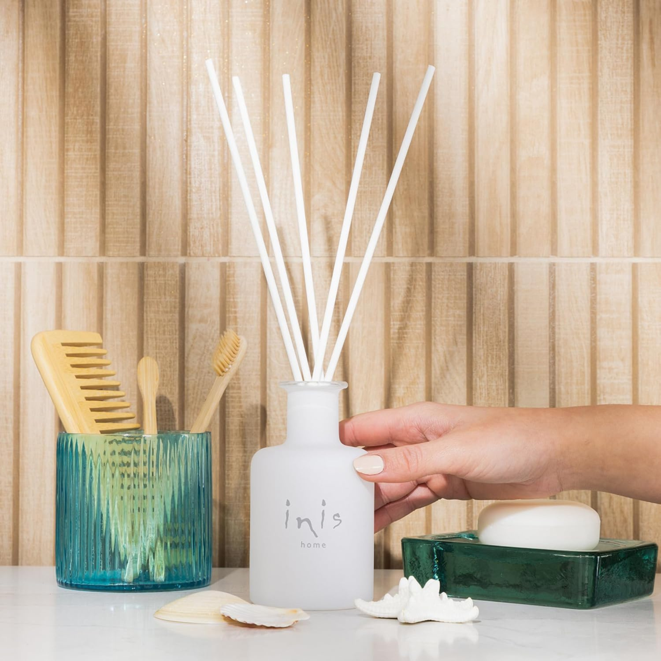Inis reed diffuser with glass bottle styled on a bathroom shelf — summer home fragrance from The Alcove Edit