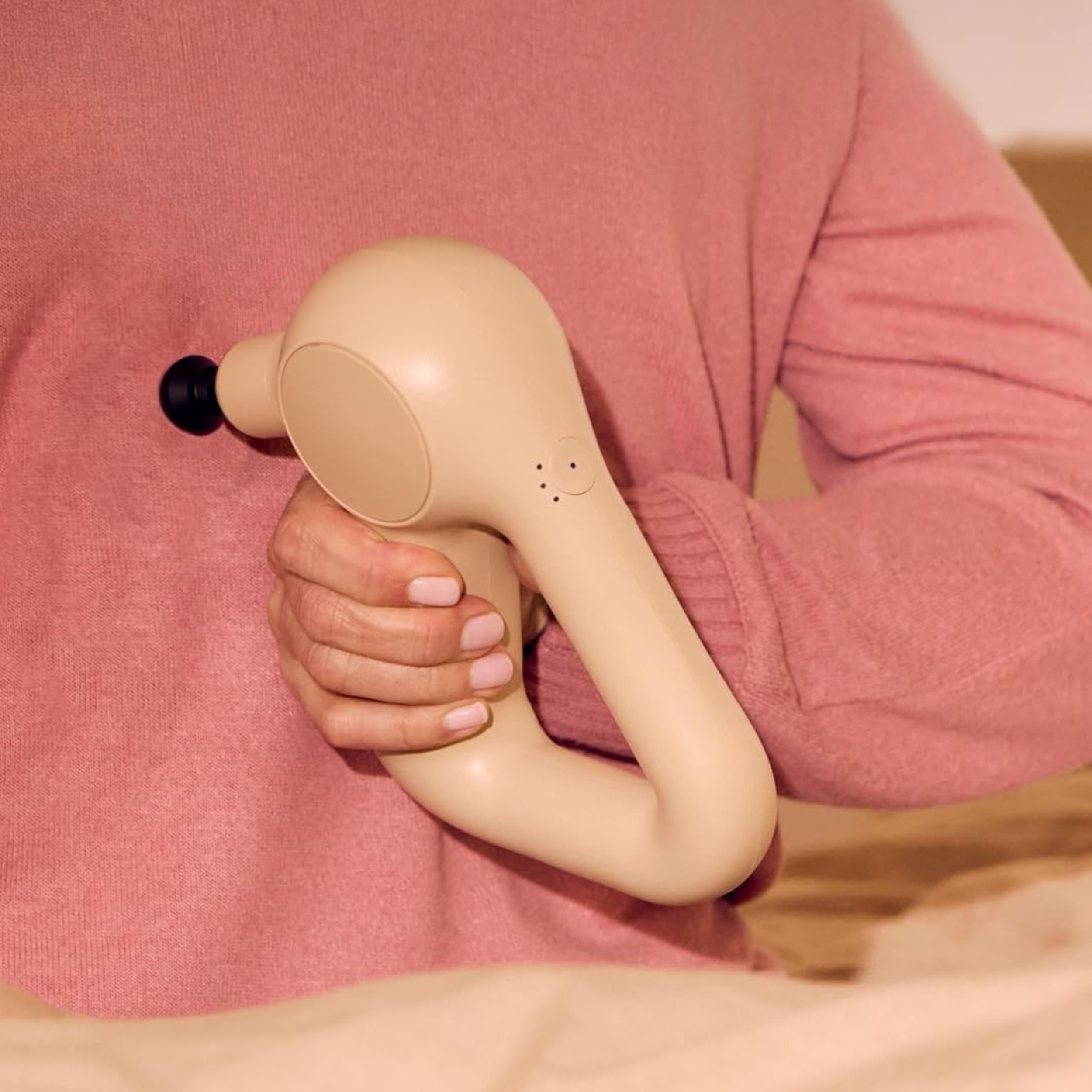 Hand holding the TheraGun Relief massage gun in sand against a soft linen background