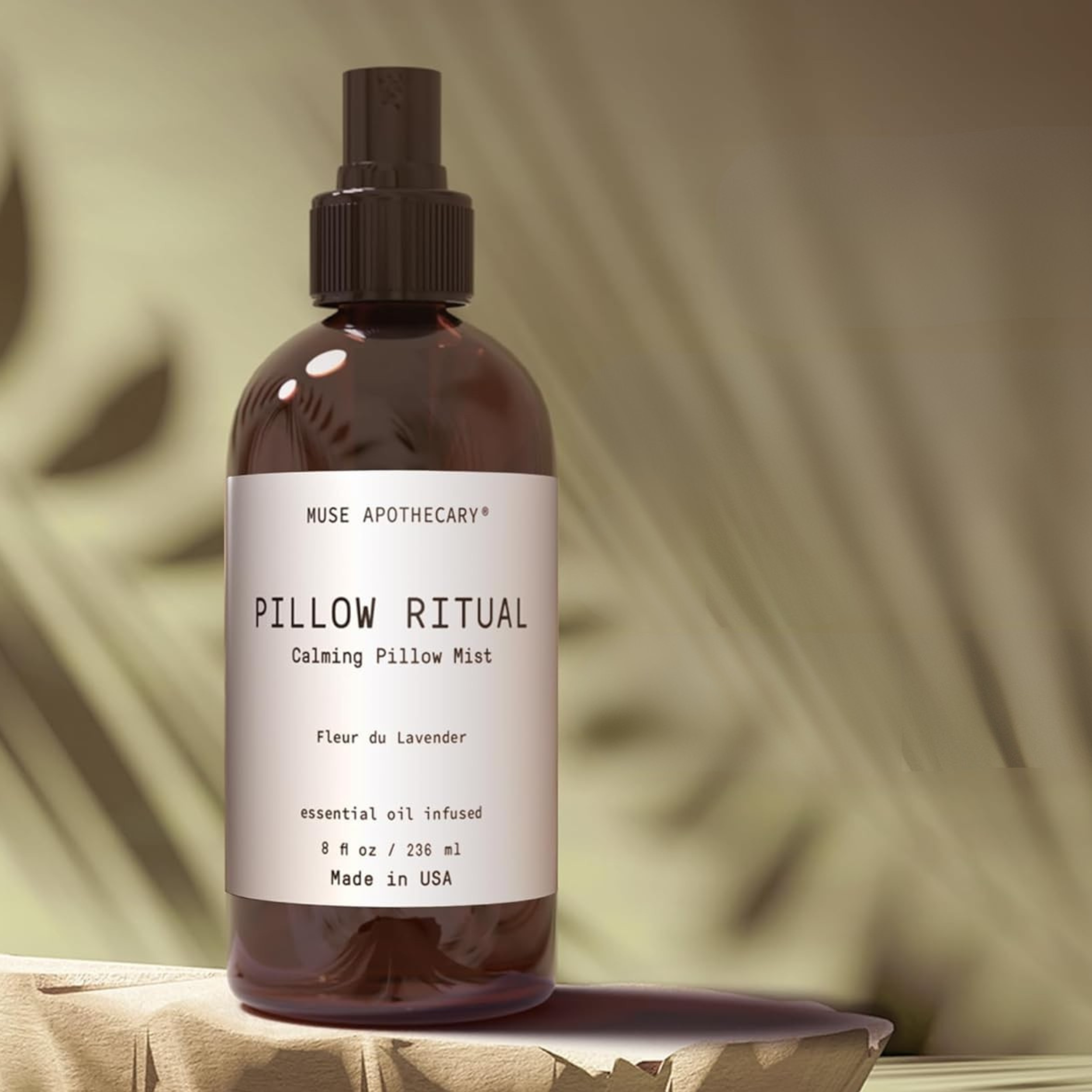 Muse Apothecary Pillow Ritual calming pillow mist in Fleur du Lavender in an amber glass bottle with pump, set on a stone surface with soft leaf shadows in the background