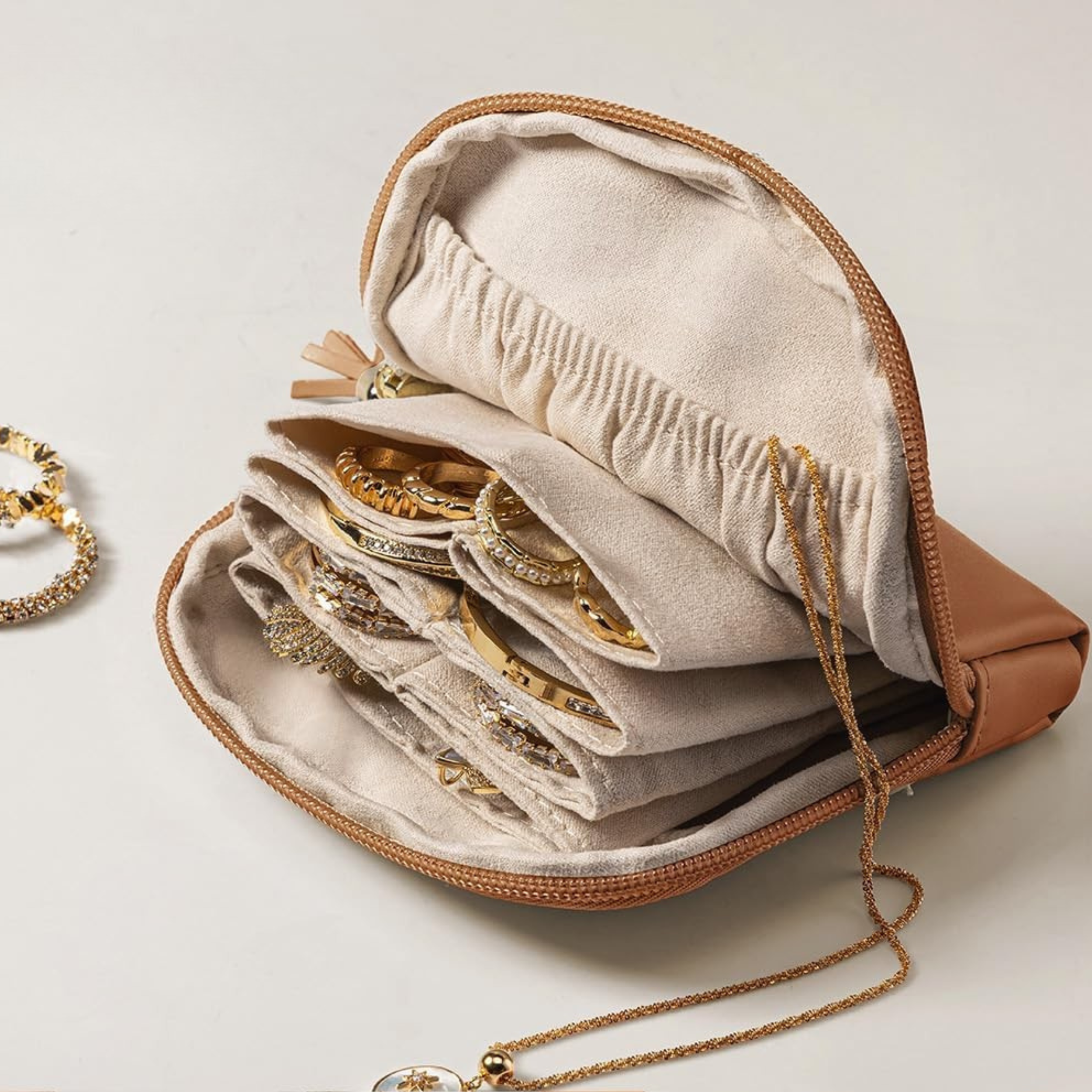 Open brown travel jewelry case lined in cream velvet, holding gold rings, bracelets, and a necklace.