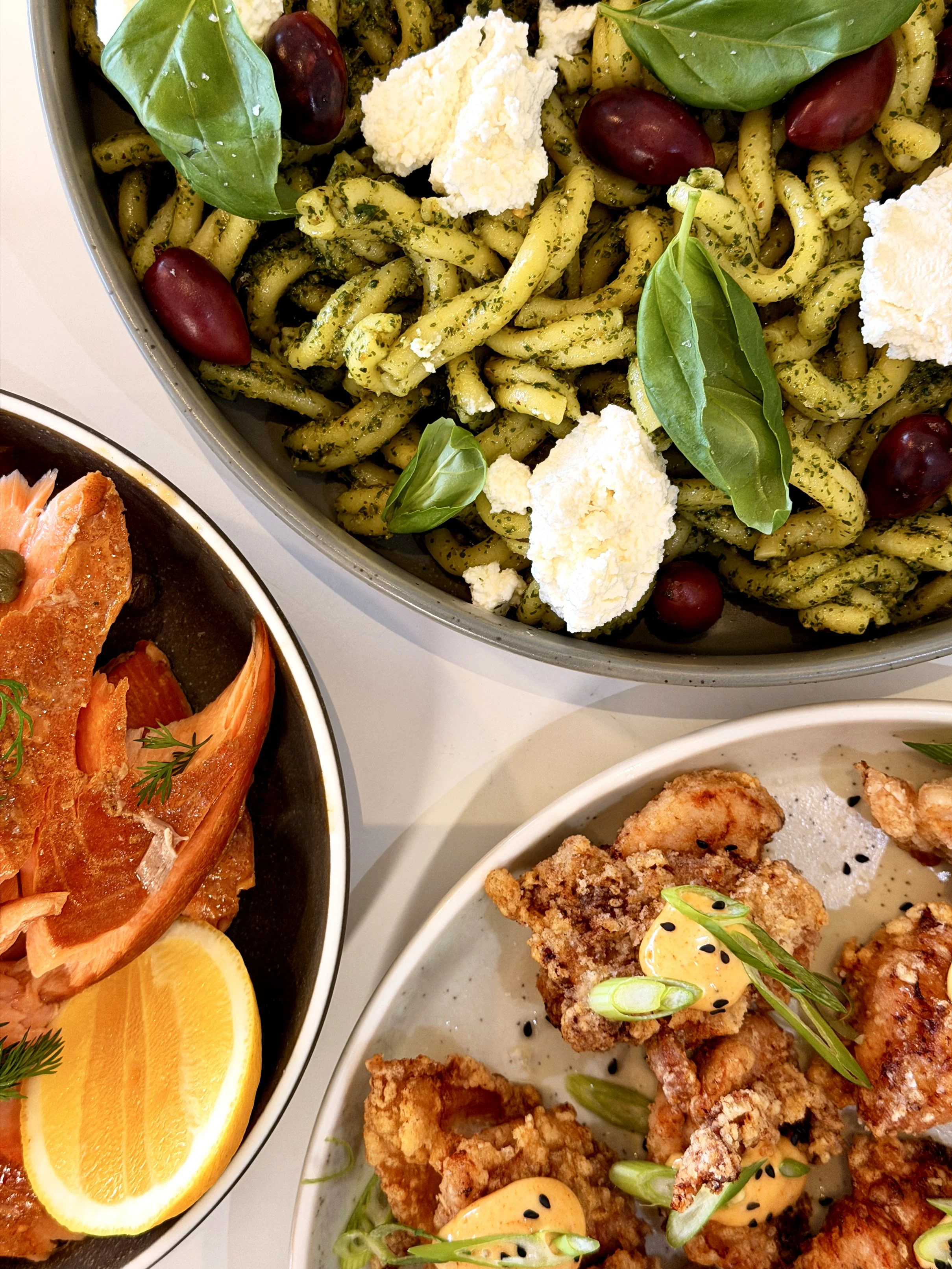 Close-up of a meal including pasta with basil, grapes, and cheese, along with other dishes with fried chicken and lemon slices.