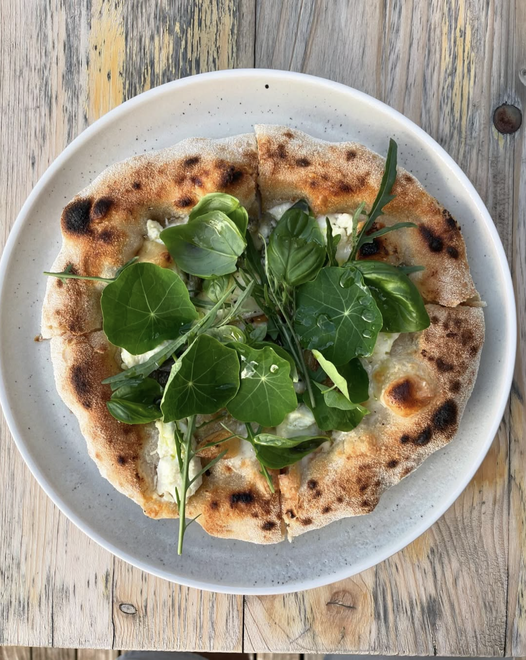 A pizza with leafy greens on top, served on a white plate placed on a wooden table.