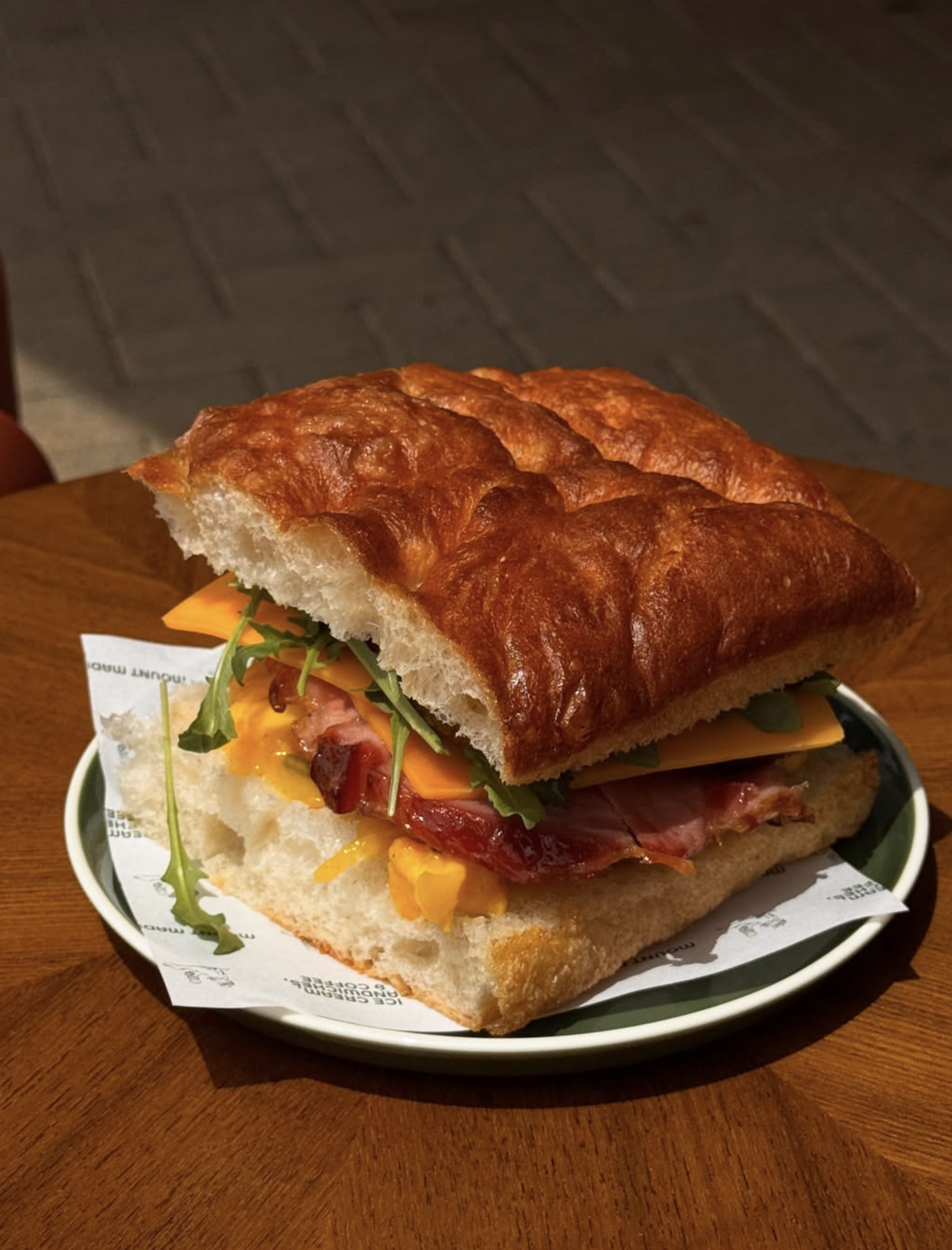 Close-up of a sandwich with bread, cheese, bacon, egg, and lettuce on a plate, on a wooden table.