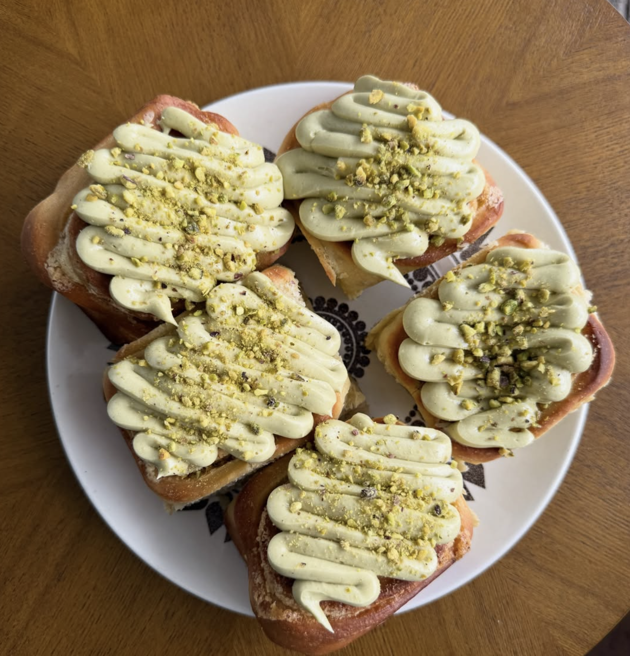 Close-up of two pieces of toast topped with green frosting and sprinkled with crushed pistachios on a white plate