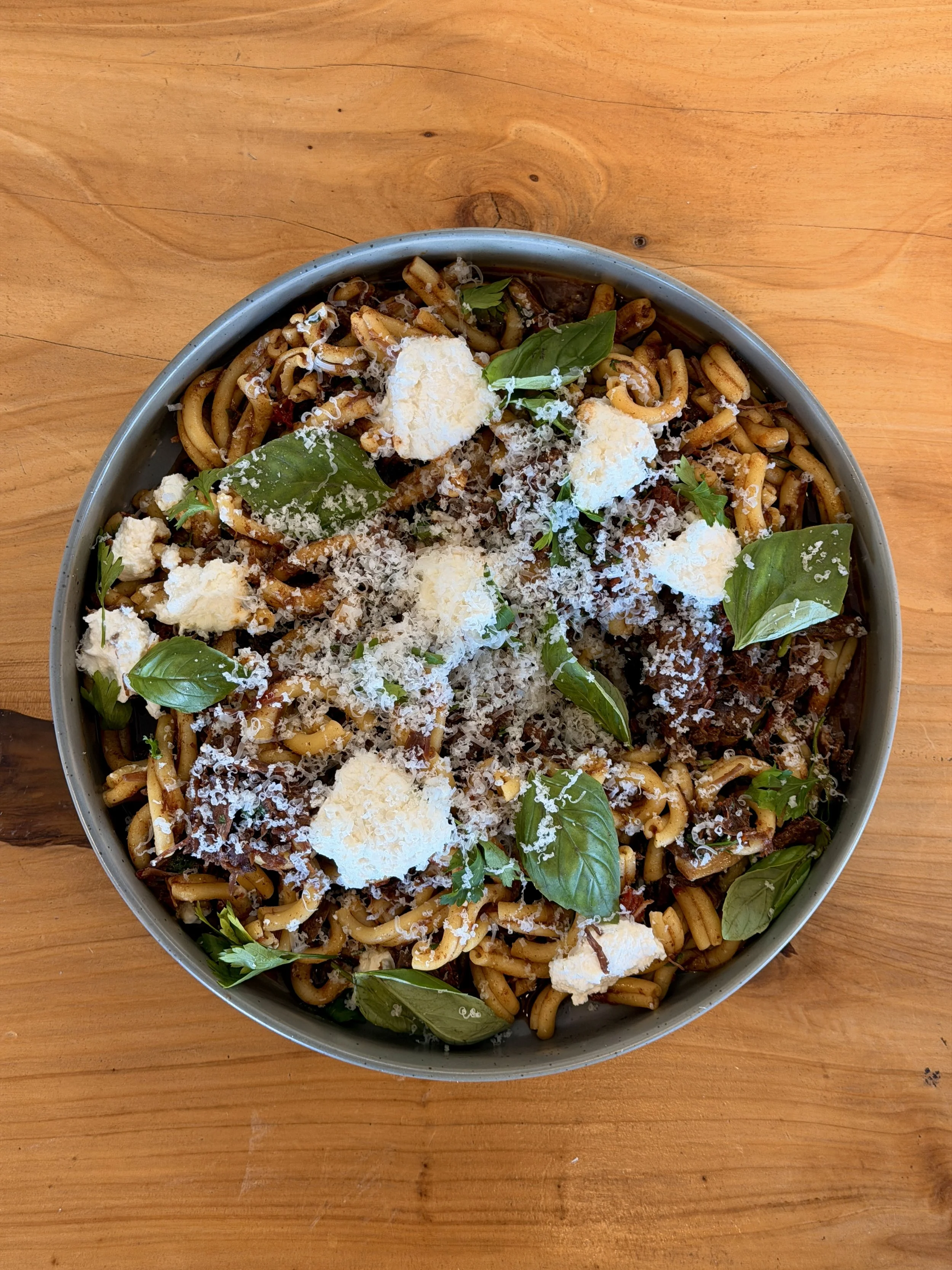 A plate of seafood pasta garnished with fresh basil leaves and grated cheese on a wooden table.