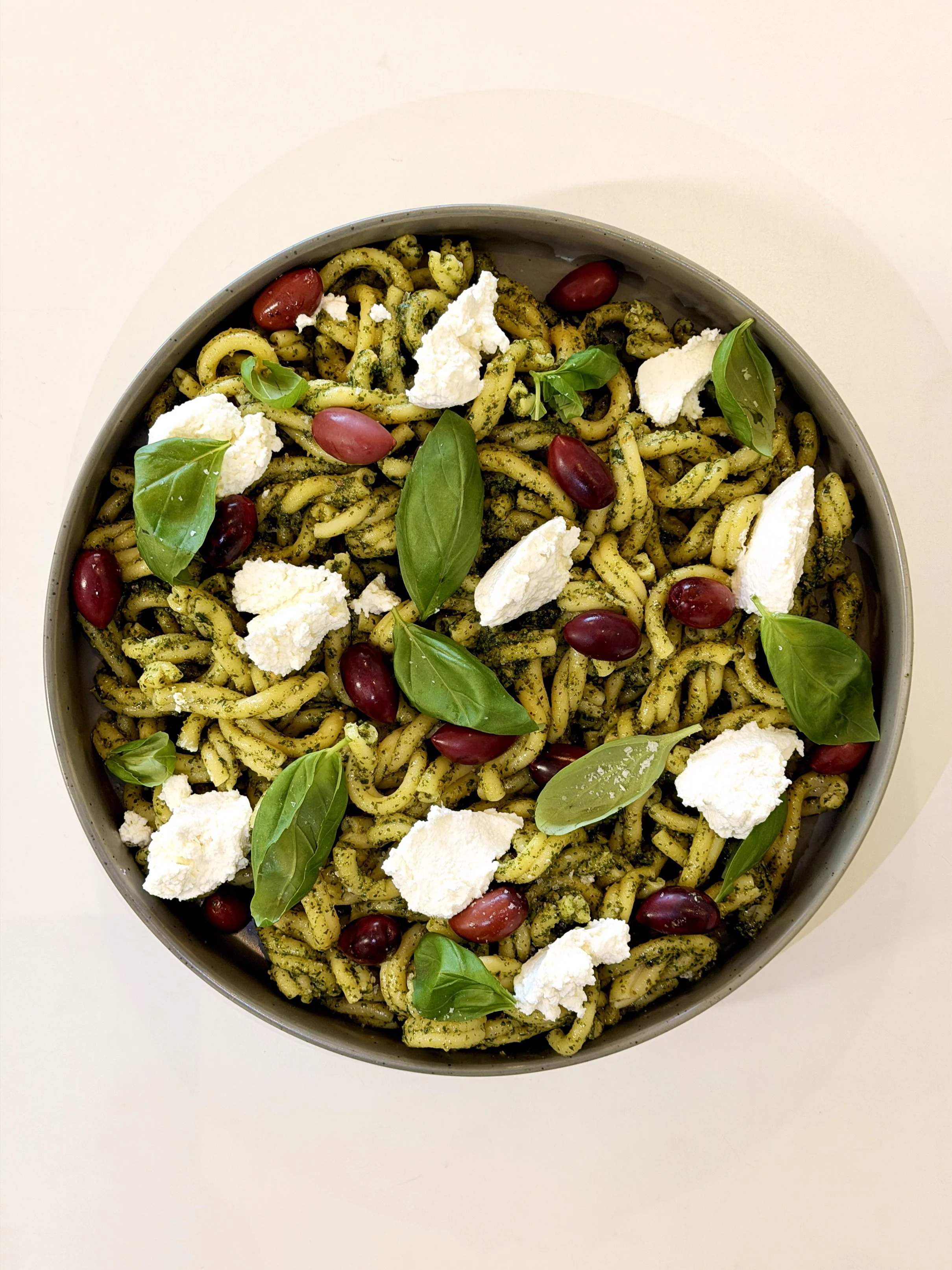 A bowl of pasta with pesto sauce, cherry tomatoes, fresh basil leaves, and chunks of mozzarella cheese.