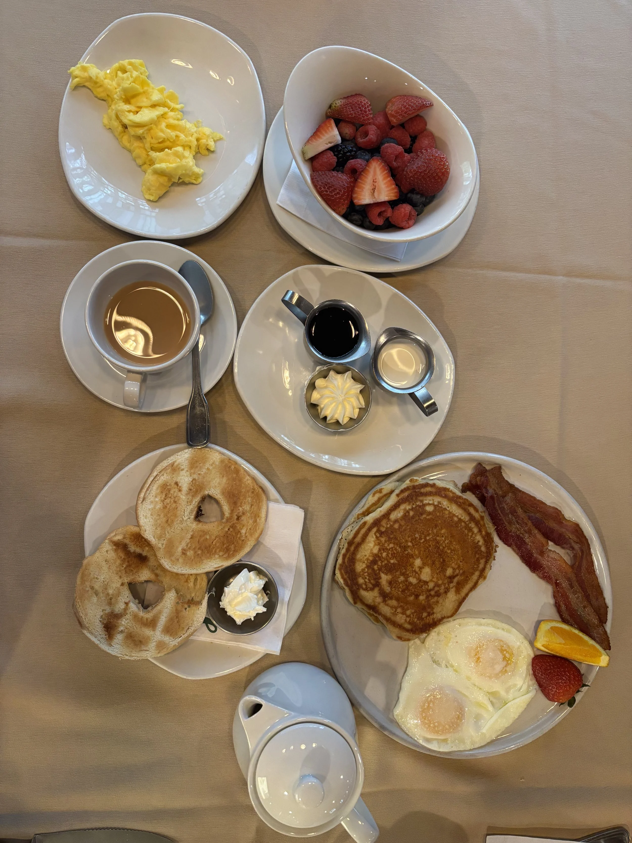 Breakfast with scrambled eggs, mixed berries, pancakes with bacon, fried eggs, toast, and coffee.
