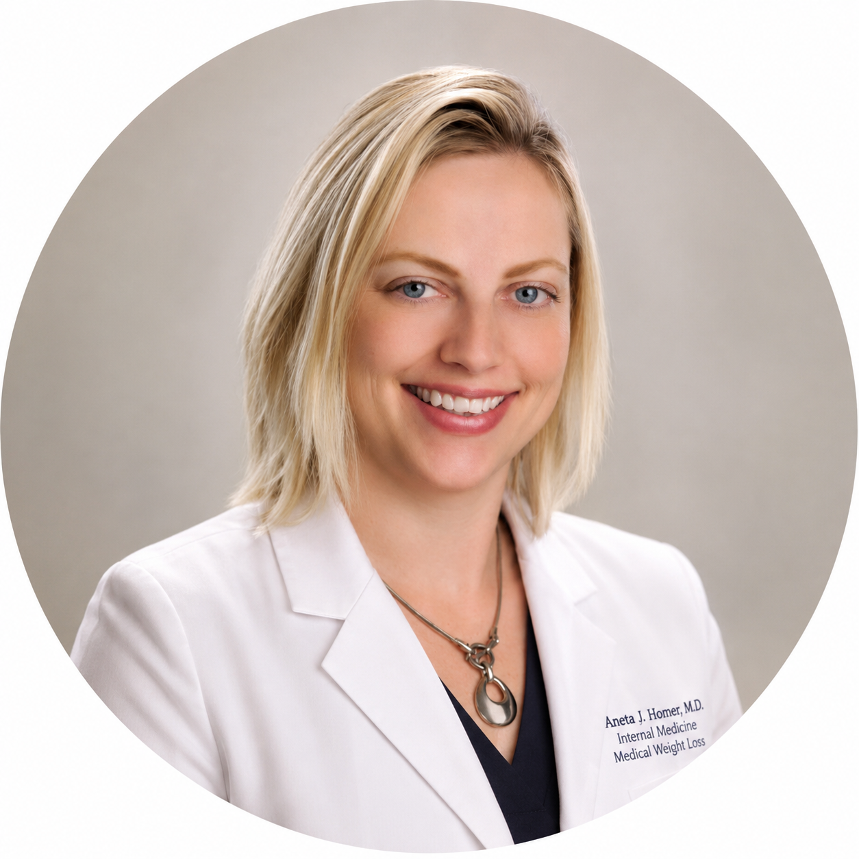 Portrait of a smiling woman with blonde hair wearing a white medical coat and a necklace, standing against a neutral background.