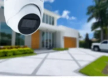 Security camera overlooking a modern house with a driveway and palm trees.