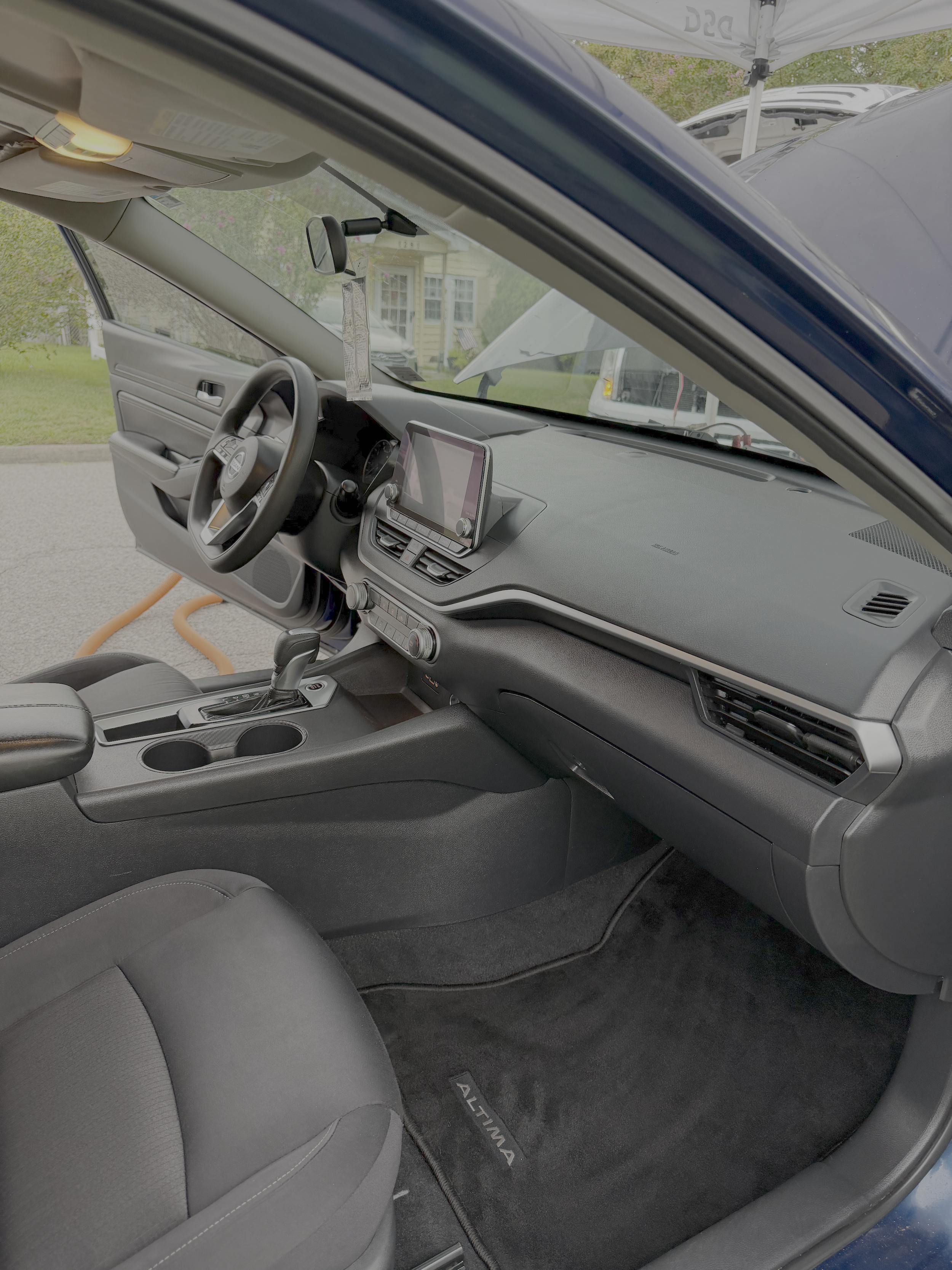 The interior of a vehicle showing the driver's side, dashboard, steering wheel, and front passenger seat. The car is parked outdoors.