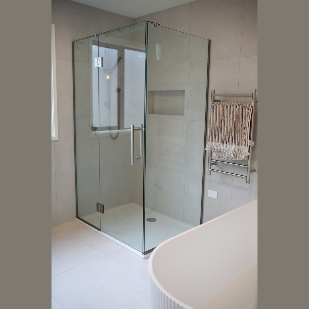 Modern bathroom with a glass shower enclosure, a built-in wall niche, a metallic towel rack with a striped towel, and a white bathtub at the edge of the image.