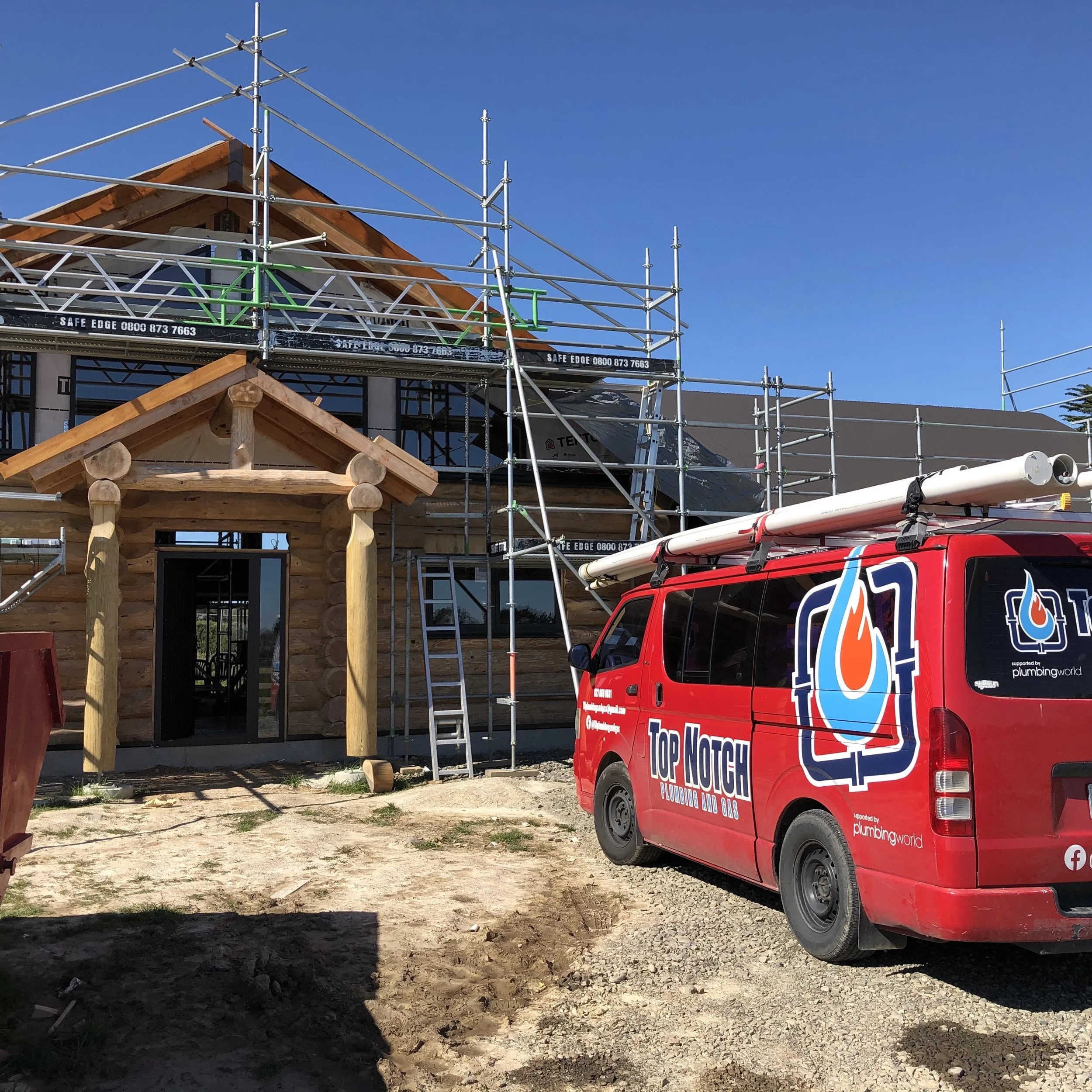 New log house under construction with plumbers van positioned to the side of the construction zone.