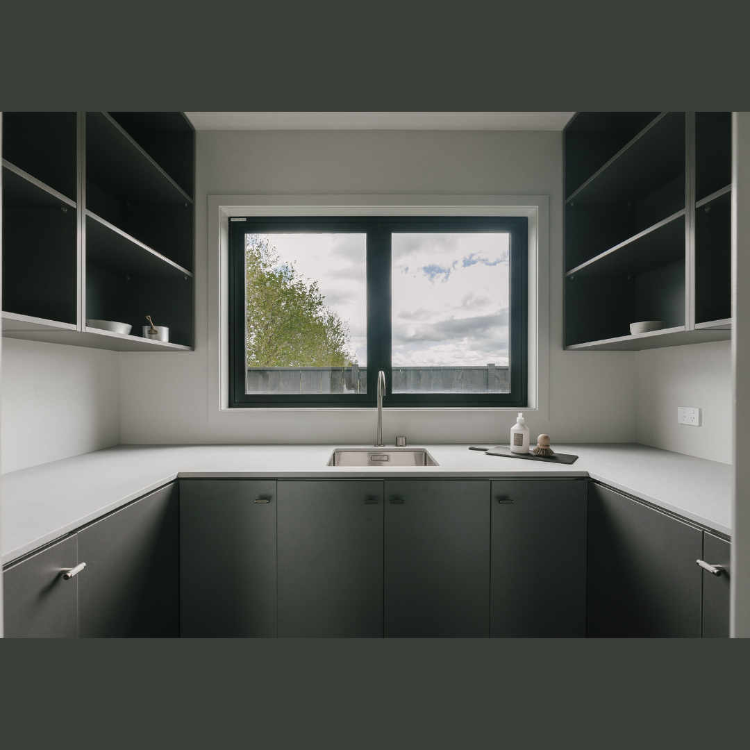 Modern kitchen with dark cabinets, a large window above the sink, and open shelves on either side, with some kitchen items on the counter.