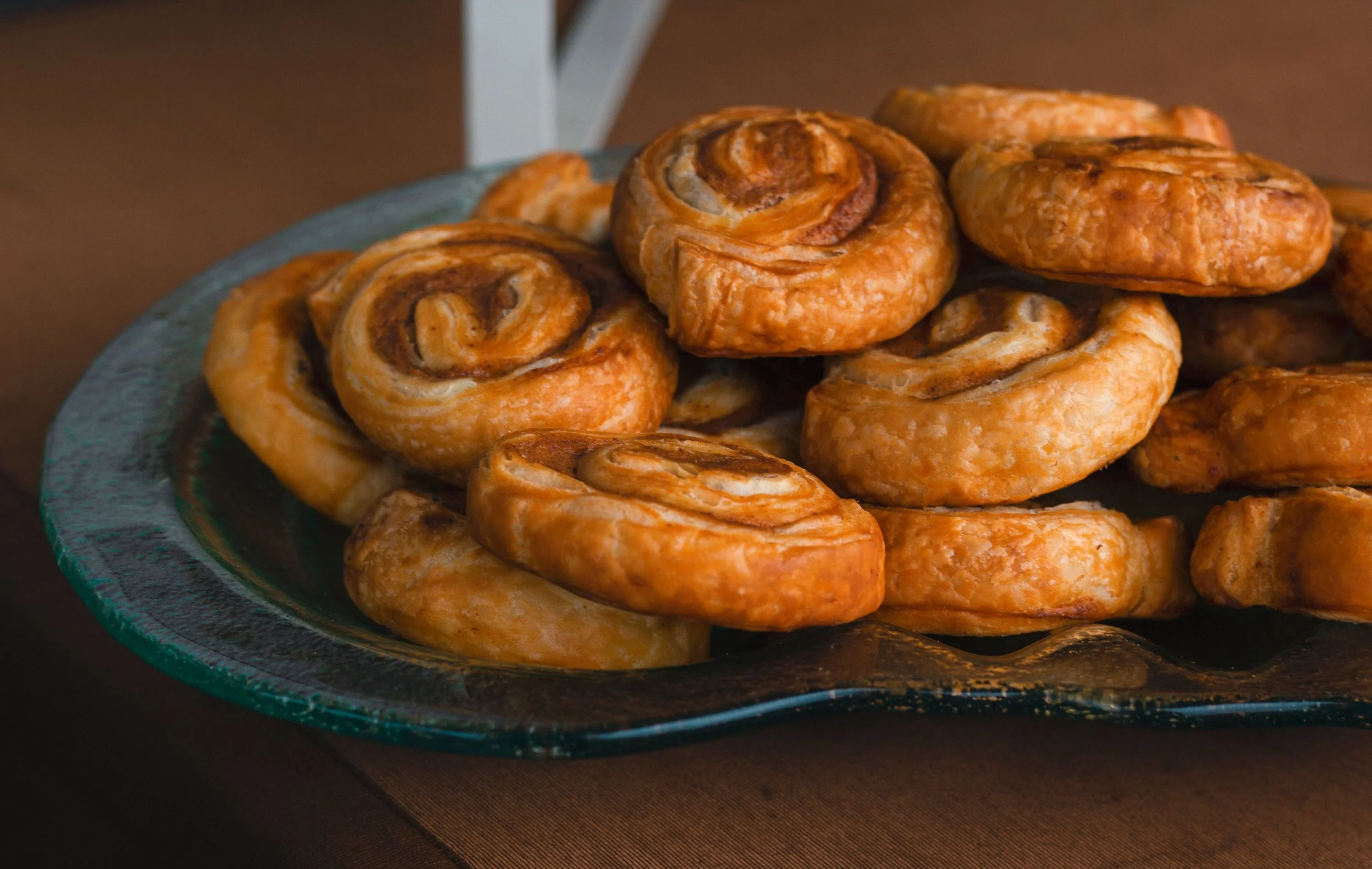 A glass plate with several cinnamon rolls stacked on top of each other, placed on a dark surface, for a corporate morning meeting