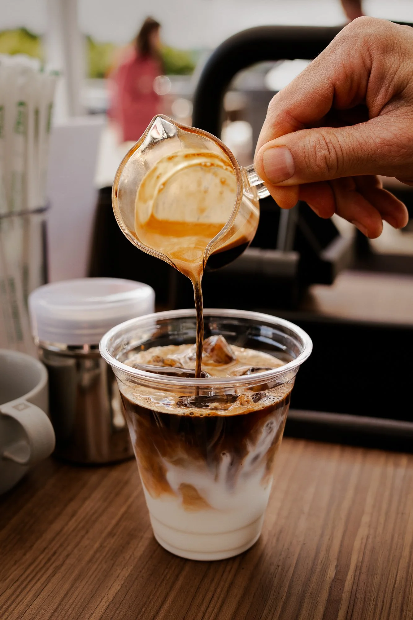 Pouring a rich espresso shot into a refreshing iced caramel macchiato.