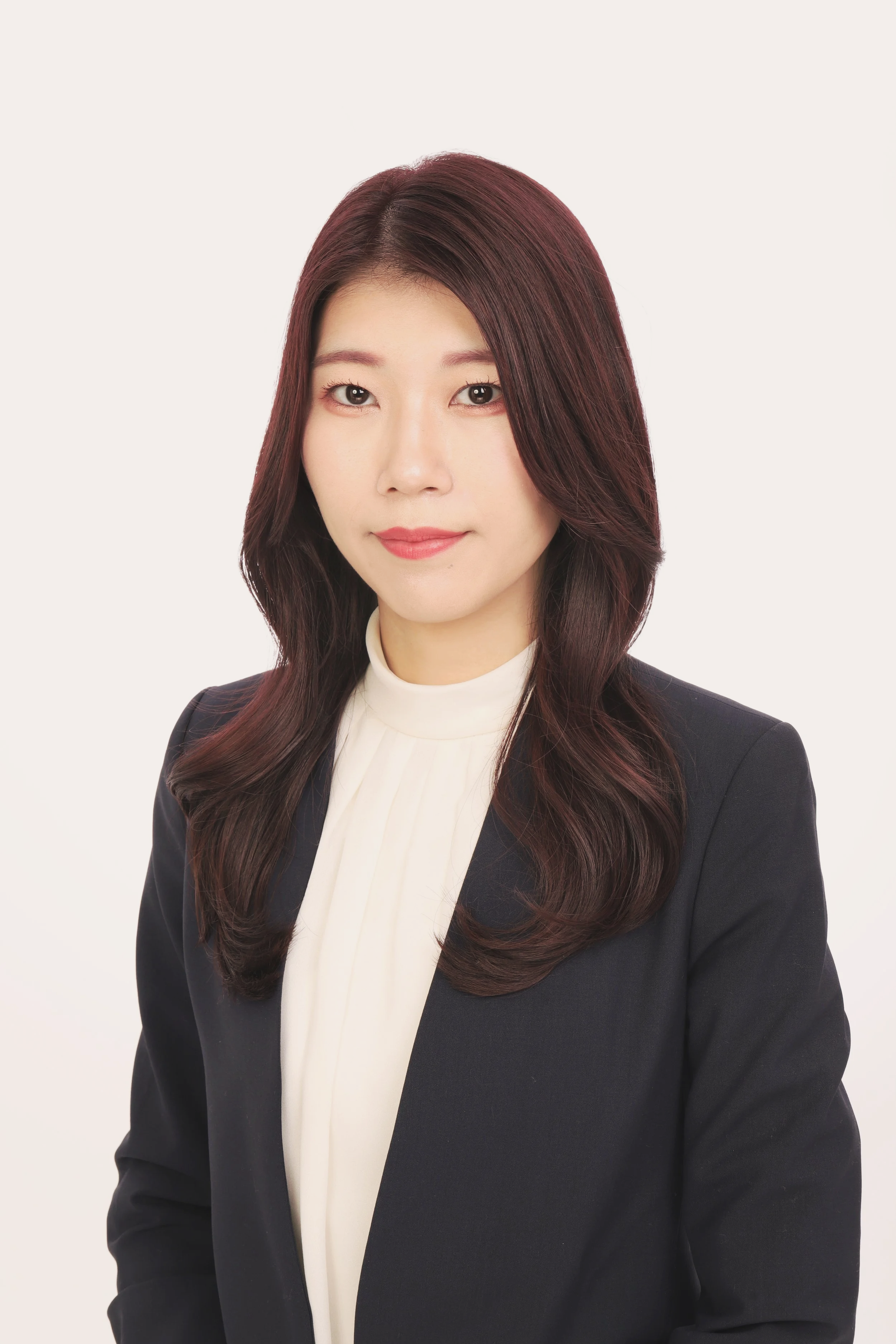 茶色の長い髪を持つ女性のポートレート。白いブラウスに黒いジャケットを着ている。背景は白色。
