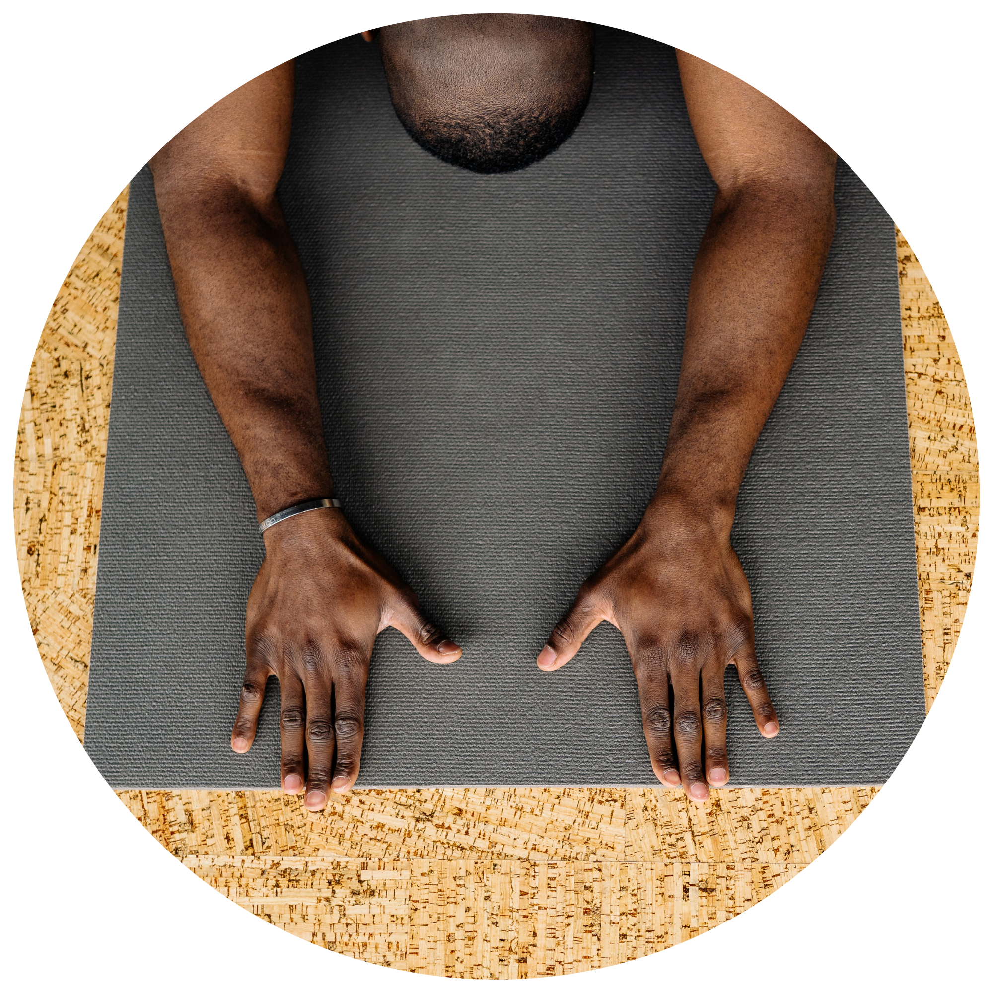 A person with dark skin lying face down on a gray yoga mat with their arms extended forward, palms down, hands relaxed.