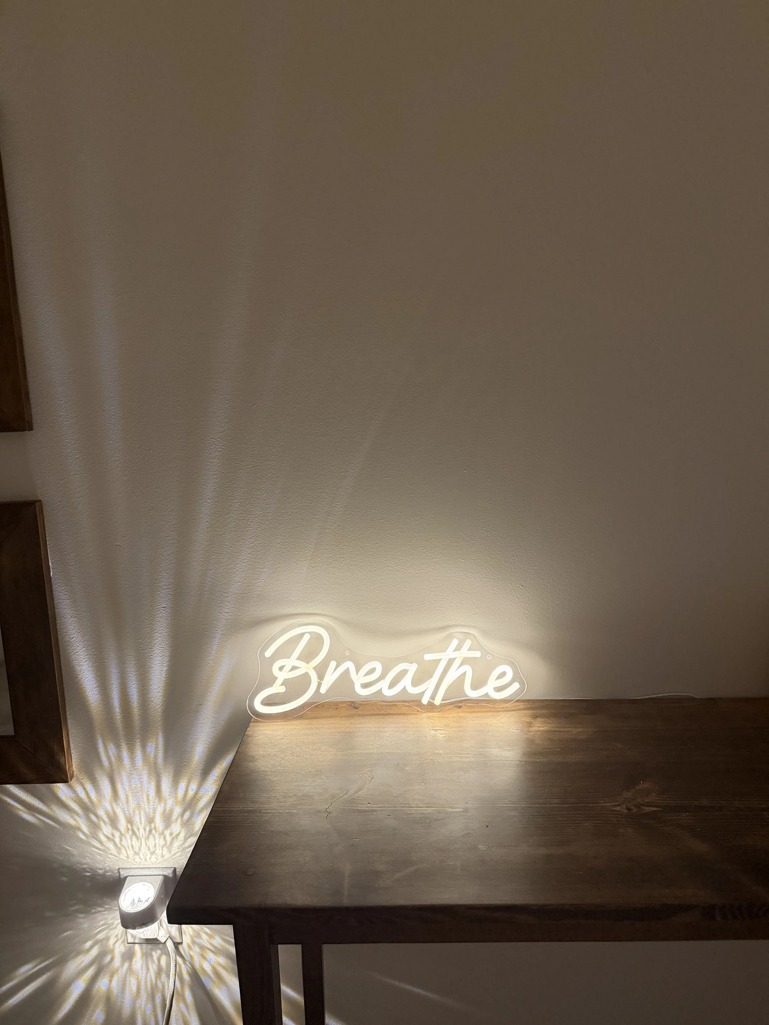 A lit neon sign spelling 'Breathe' on a wall, casting patterned light shadows on the wall and floor.