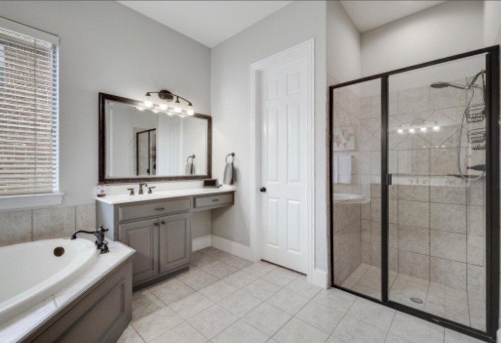 Bathroom with a bathtub, double sink vanity, mirror, and a glass-enclosed shower.