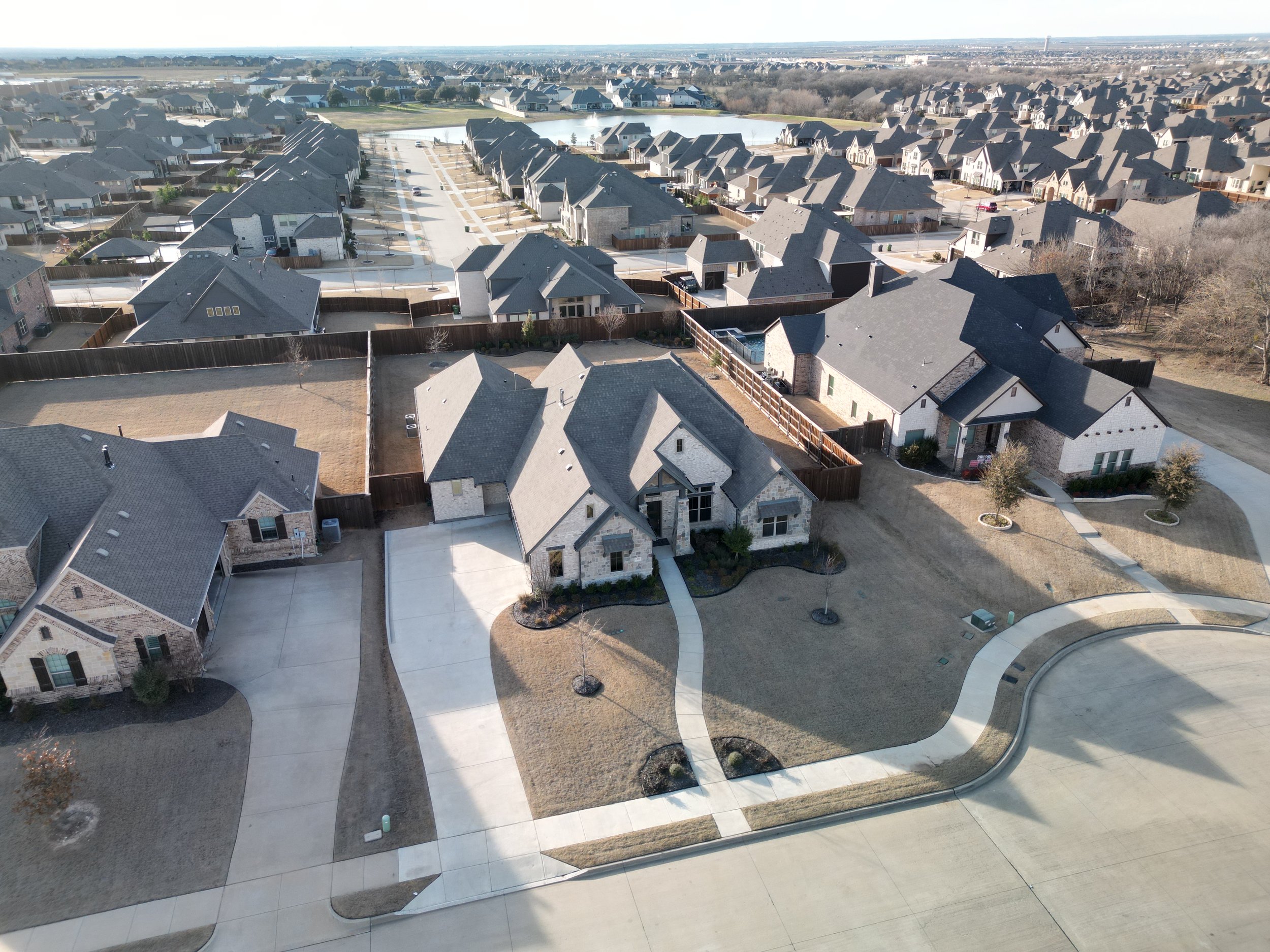 Aerial view of a suburban neighborhood with houses, roads, a pond, and open spaces.