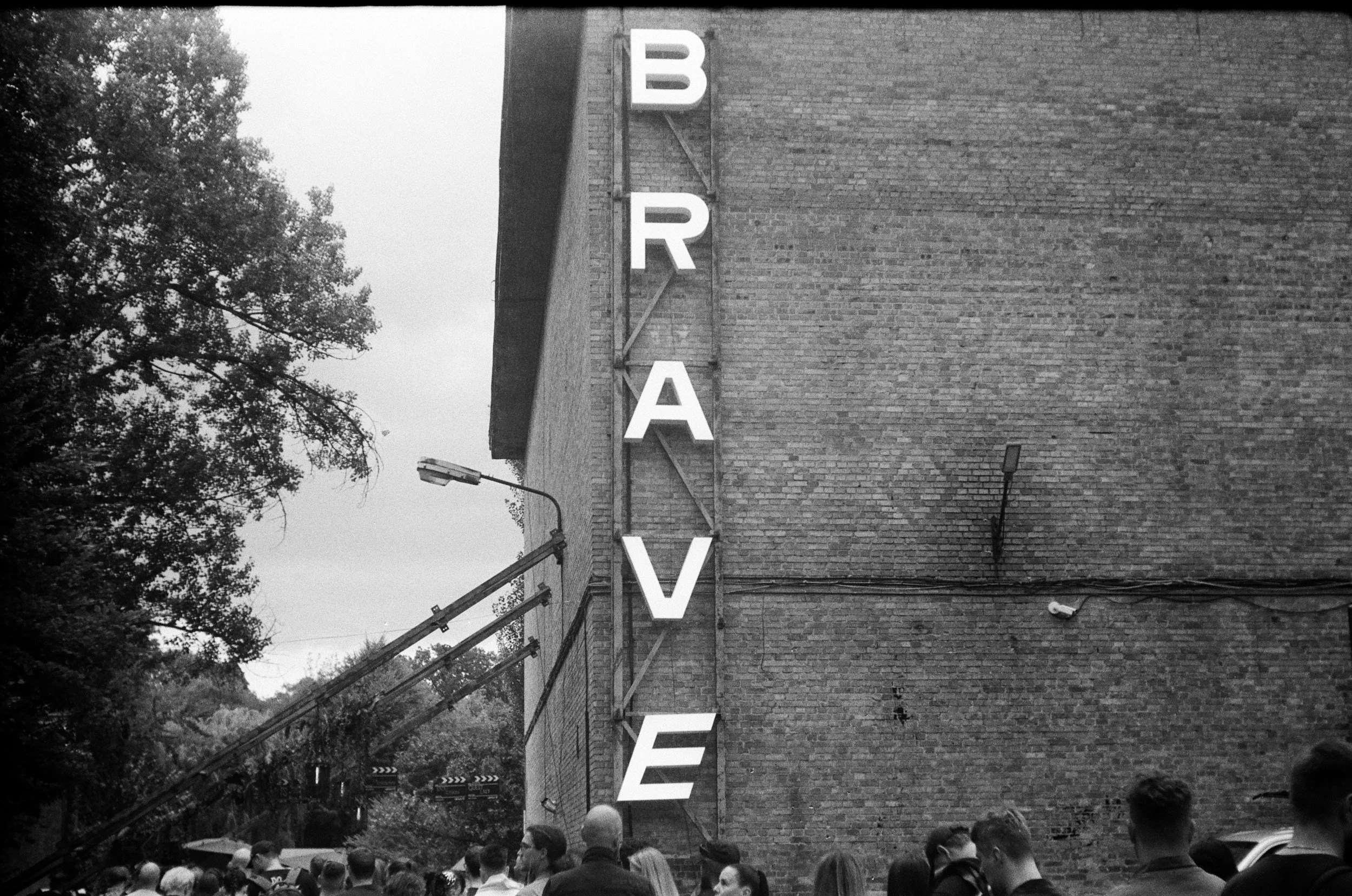 Black and white photo of a brick building with large vertical letters spelling 'BEAVER'. The crowd is gathered underneath, with trees visible in the background.