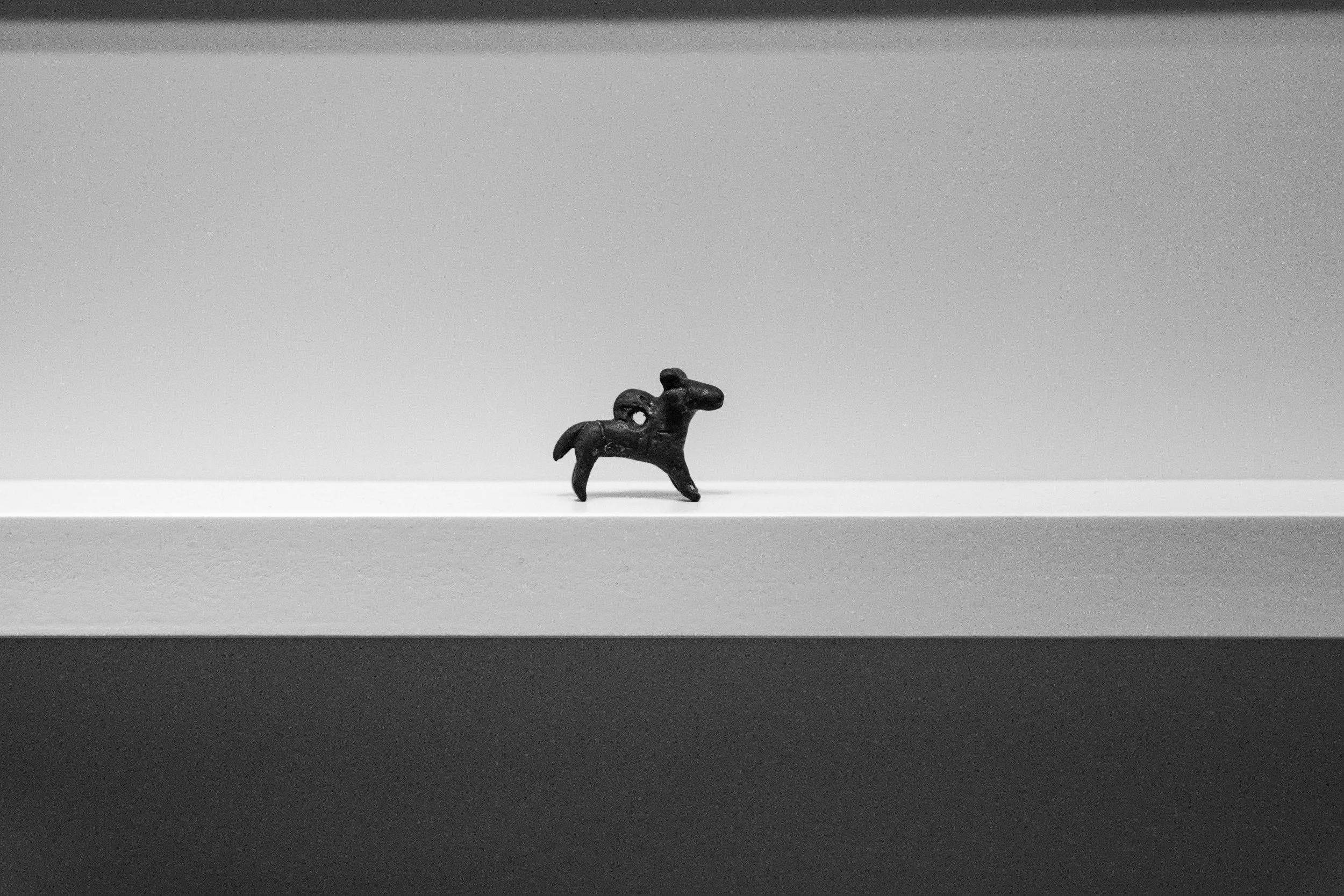 Small black figurine of a horse on a minimalist white shelf, with a gray background.