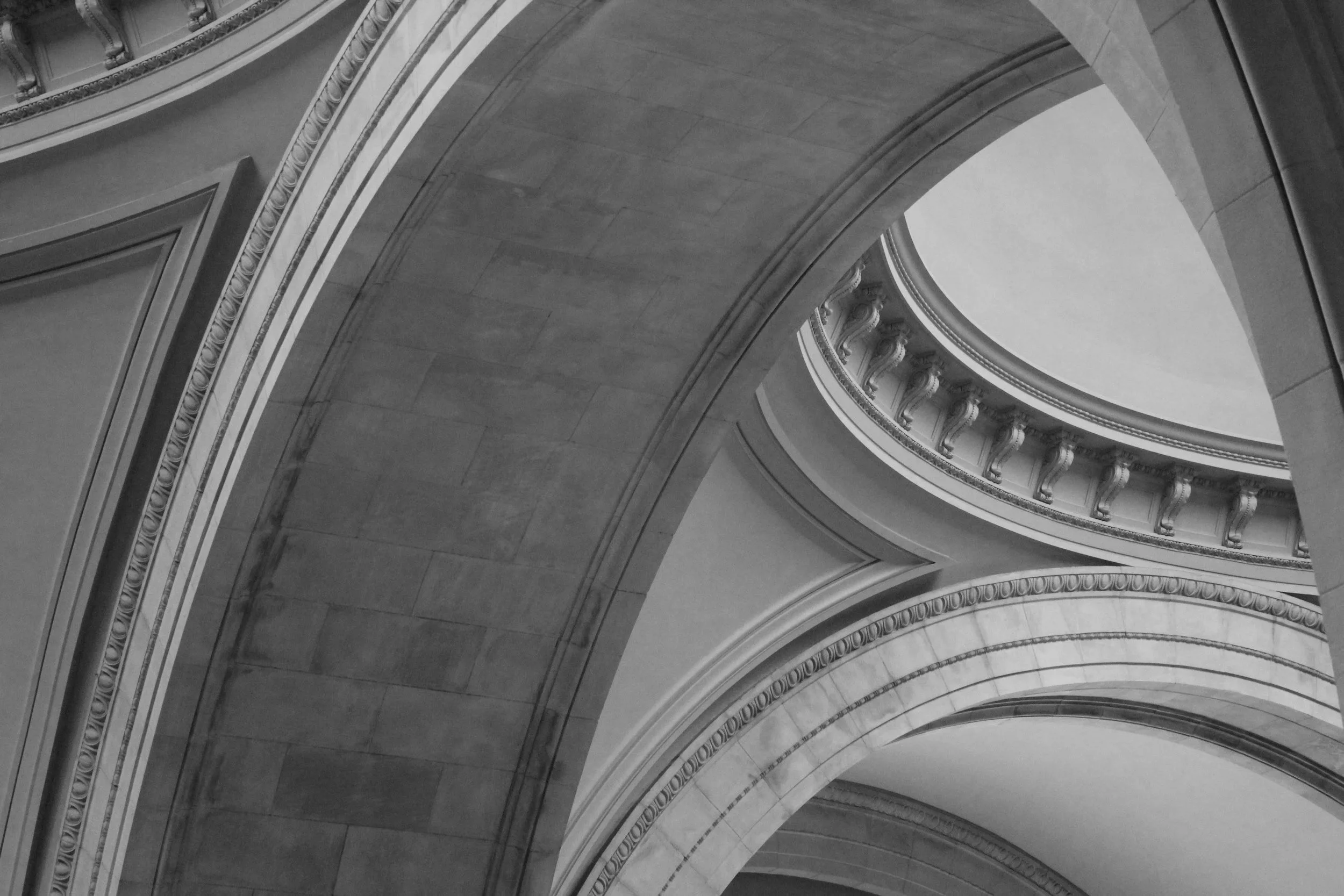 Black and white photograph of the interior of a domed building, showcasing ornate architectural details and columns supporting the curved structure.
