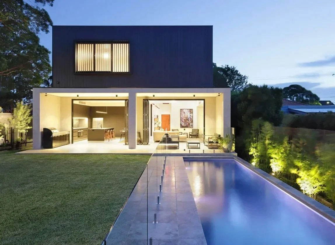 Modern two-story house with an outdoor pool, illuminated interior, and landscaped backyard at dusk.